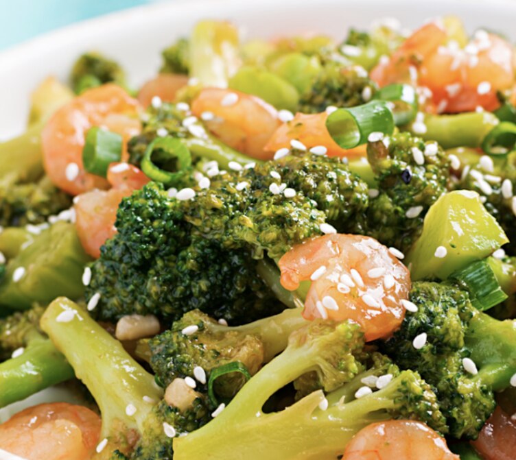 Shrimp and broccoli stir fry topped with sesame seeds on a white plate with chopsticks