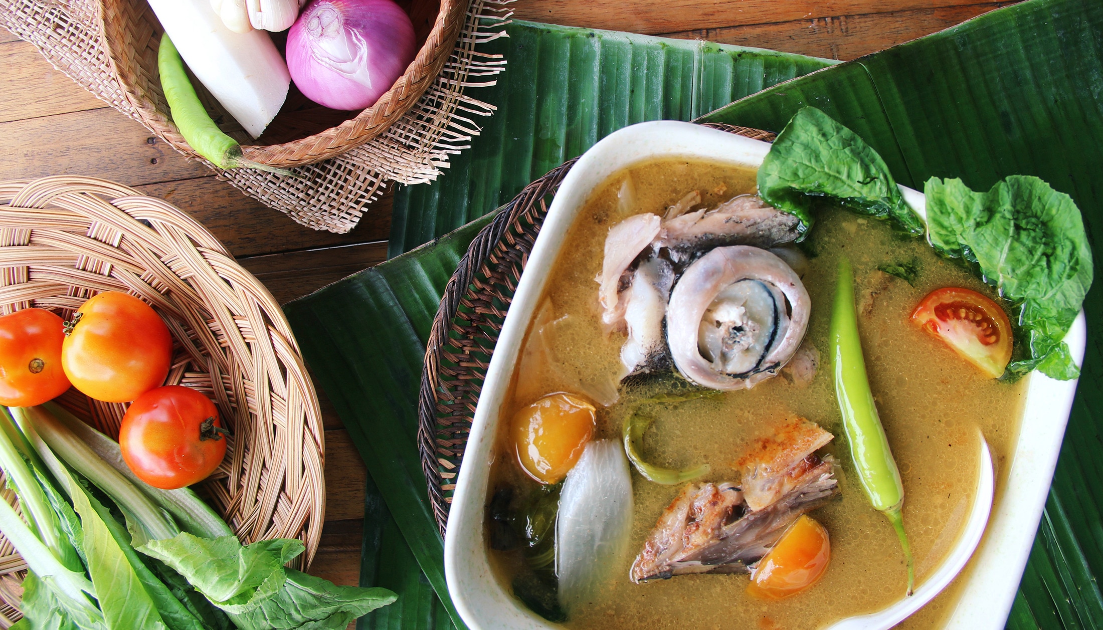 A bowl of fish sinigang surrounded by fresh ingredients