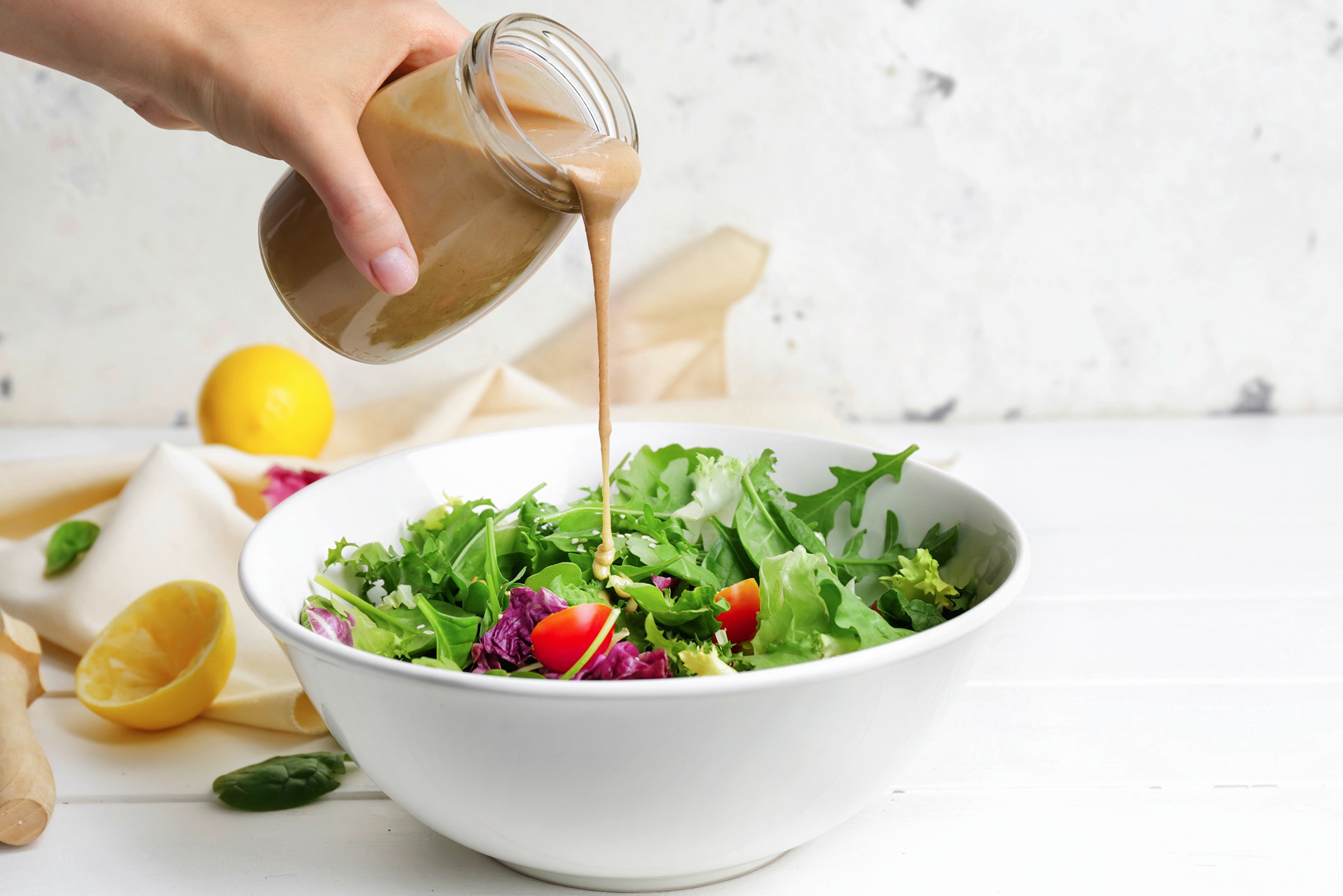 A person pours dressing into a bowl of fresh salad greens