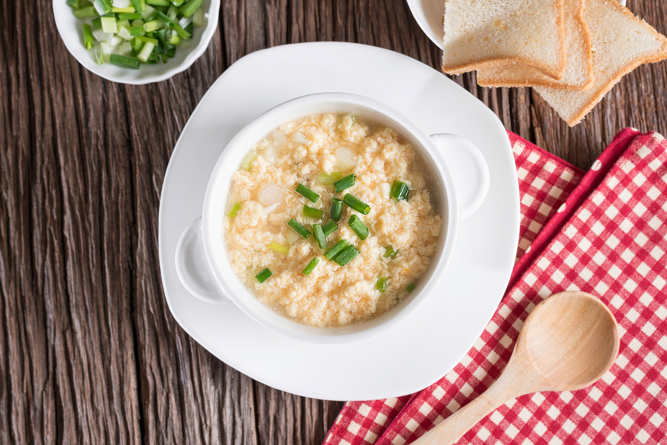 A bowl of egg drop soup garnished with scallions