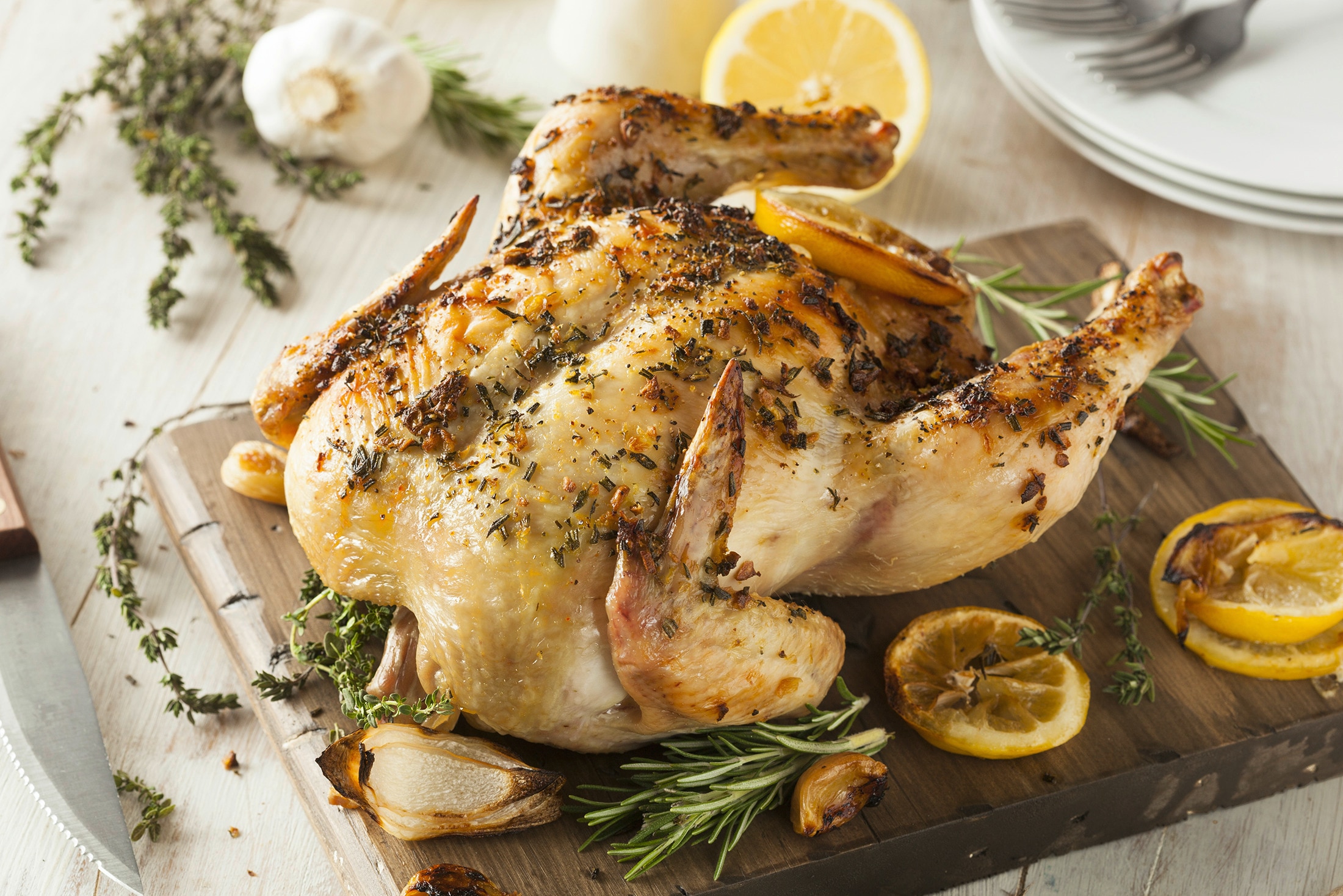 A cutting board with a whole baked chicken garnished with herbs