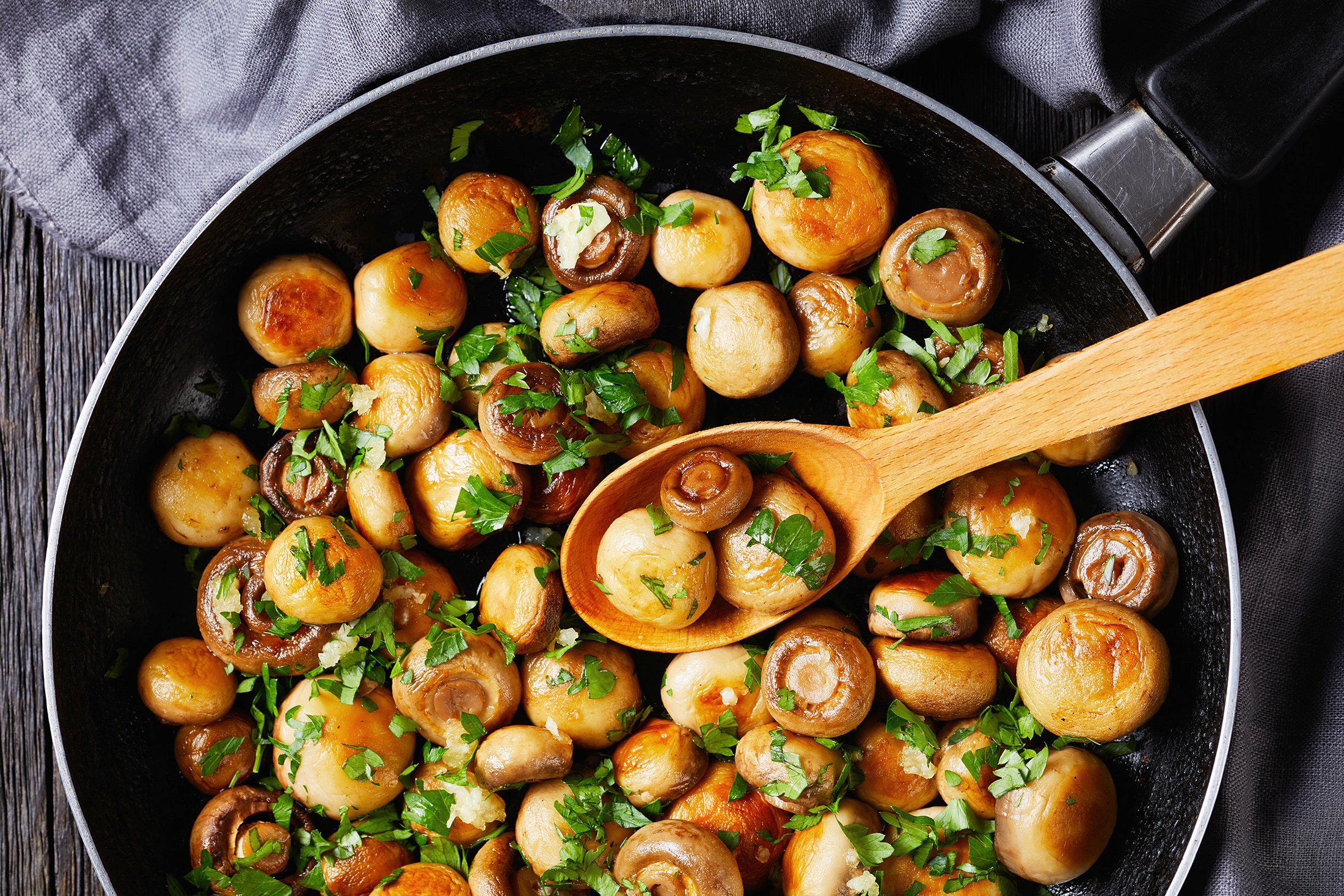 A frying pan with button mushrooms in garlic and herbs