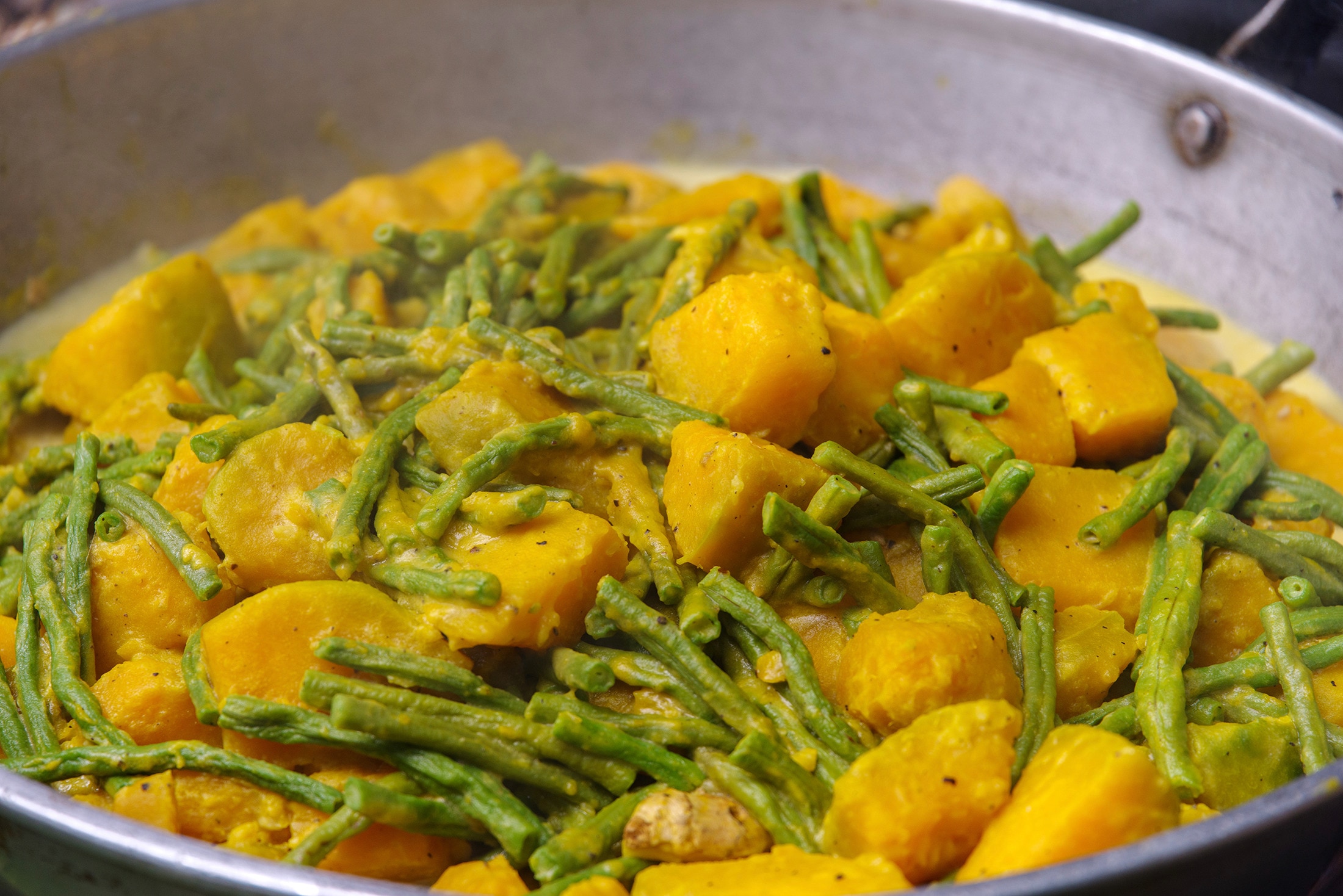 A large pan with squash and string beans in coconut milk