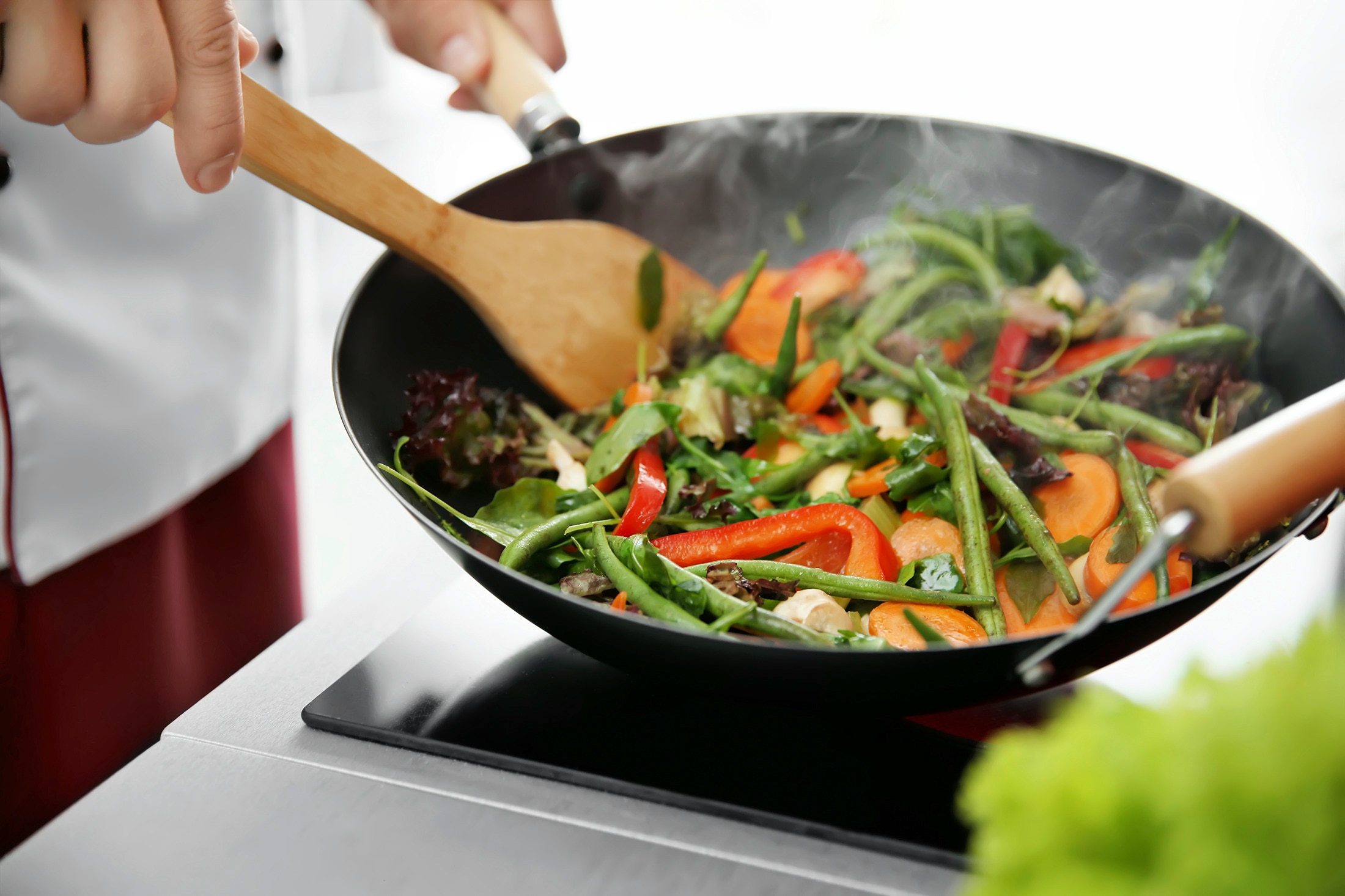 A cook tossing vegetables in a searing hot wok