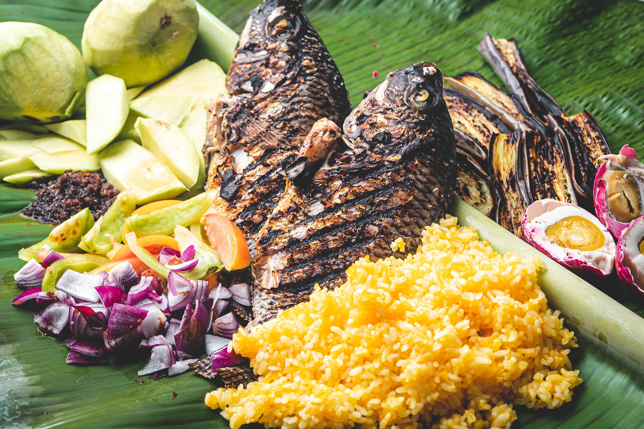 Grilled fish with green mangoes, salted egg, and rice on a banana leaf