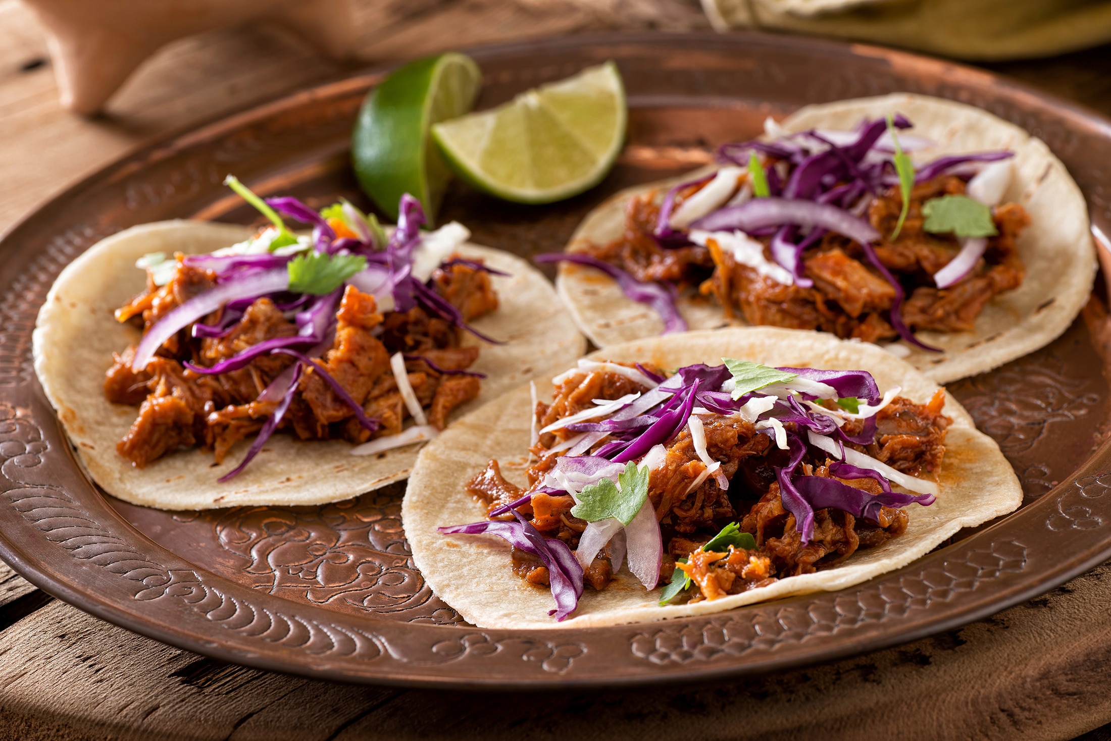 Three pulled pork soft tacos topped with shredded cabbage and cilantro
