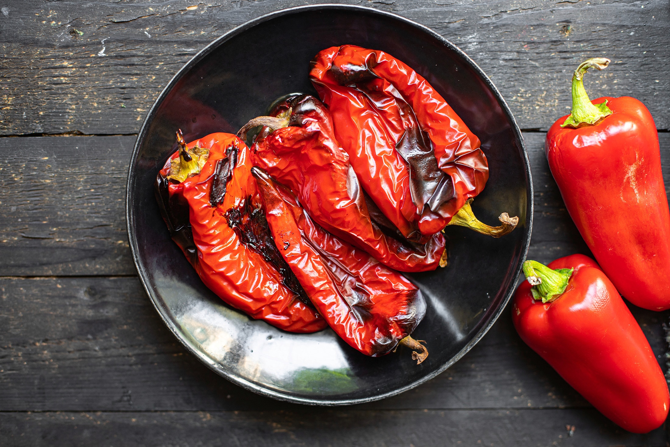 A plate of roasted red bell peppers on a dark wooden tabletop