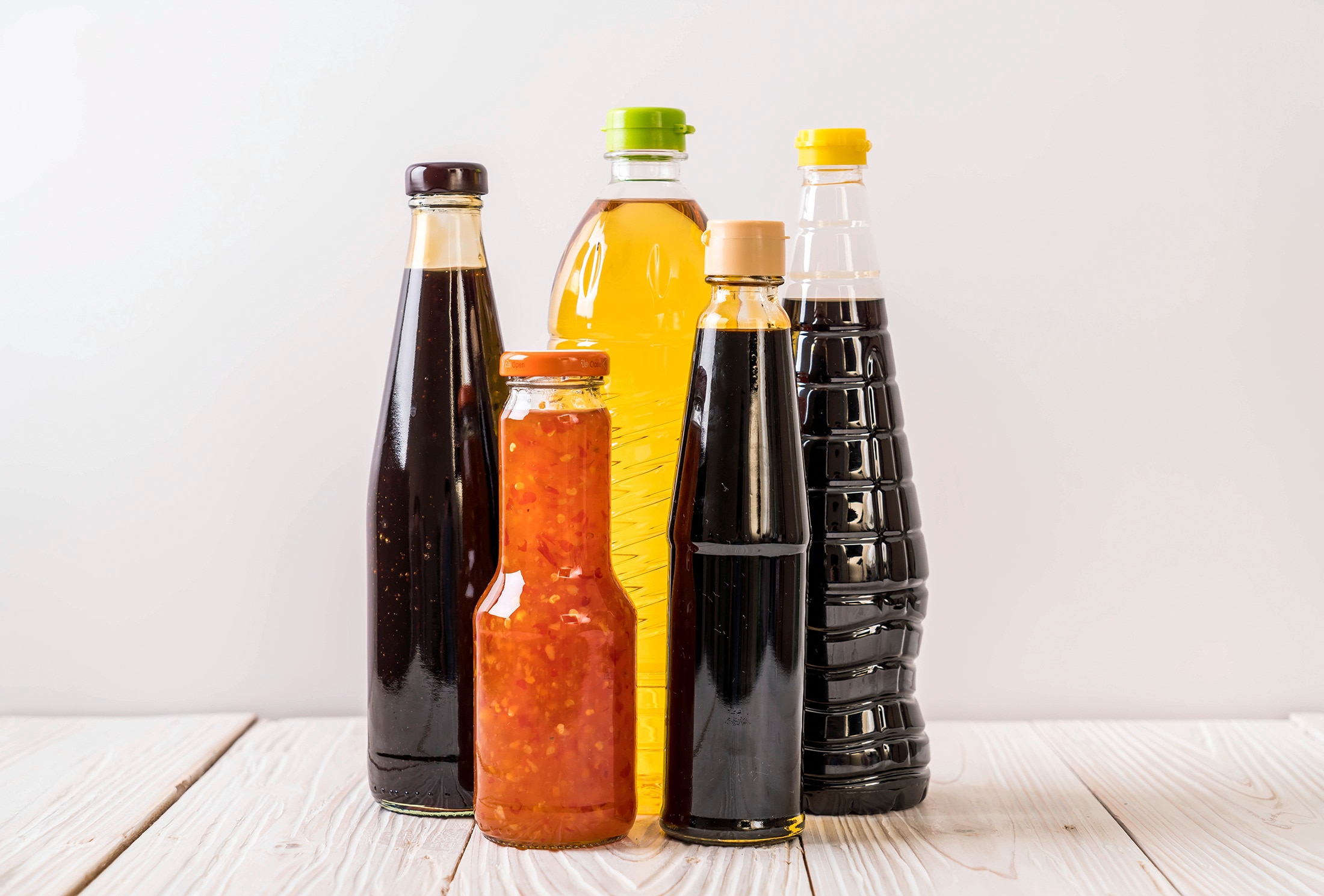 A selection of bottled condiments on a light wooden countertop