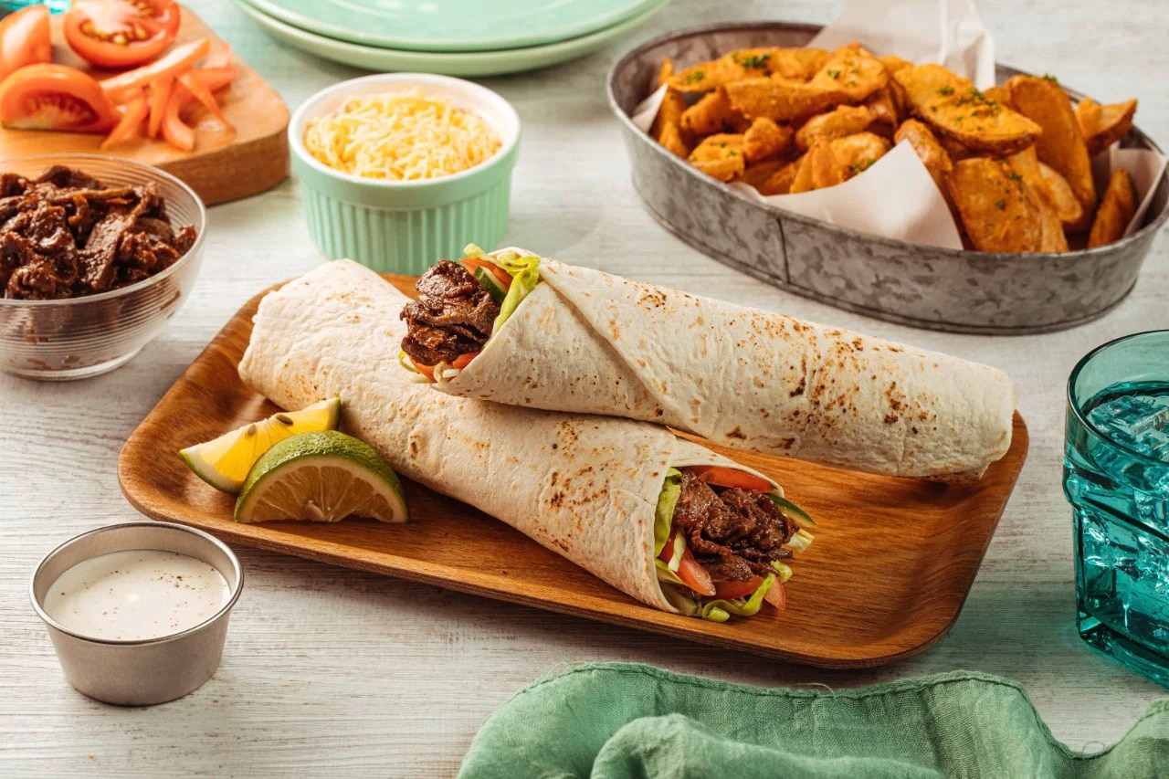 Two beef shawarma wraps on a wooden tray