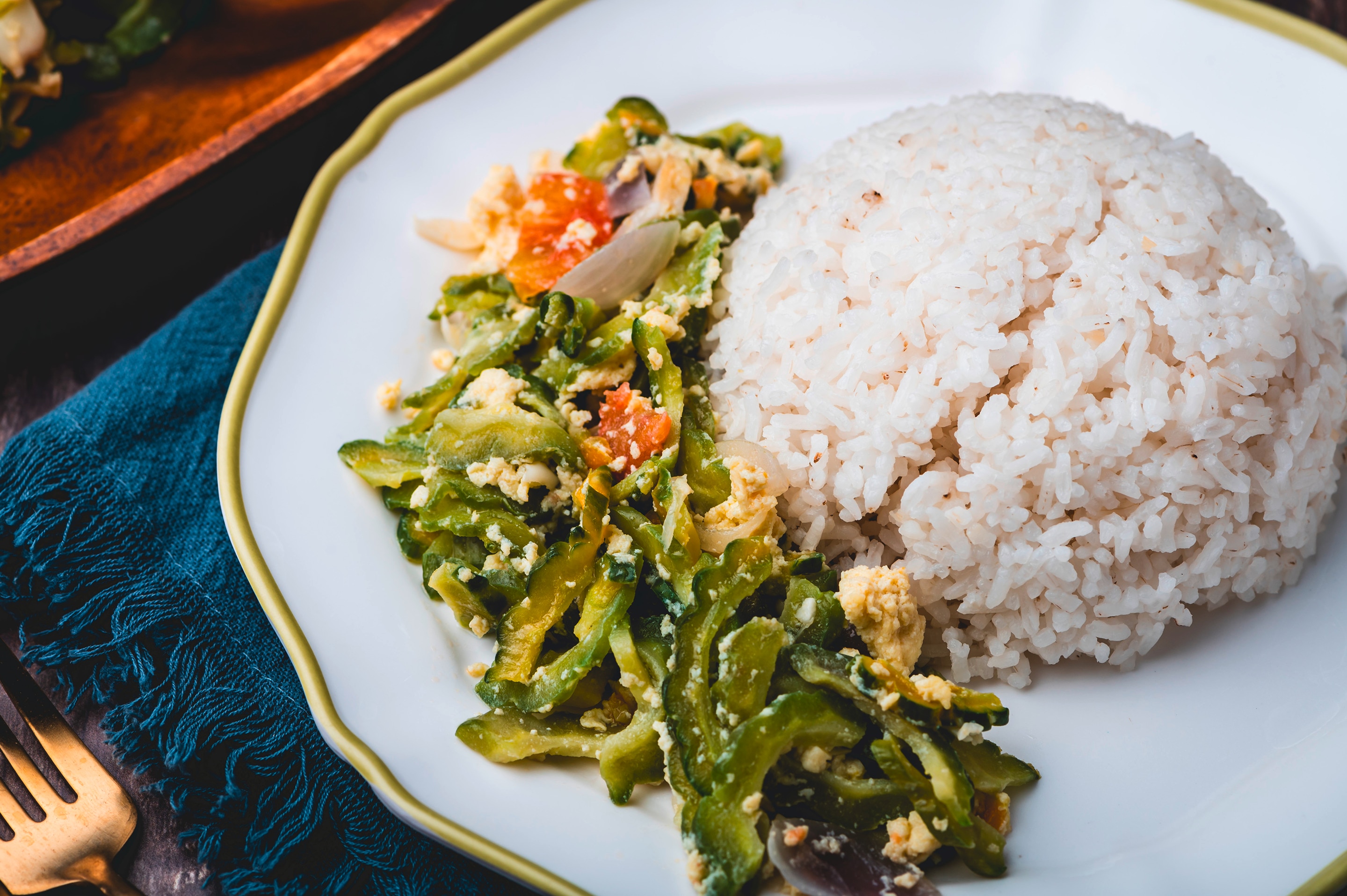 A plate with ginisang ampalaya with egg and a cup of rice