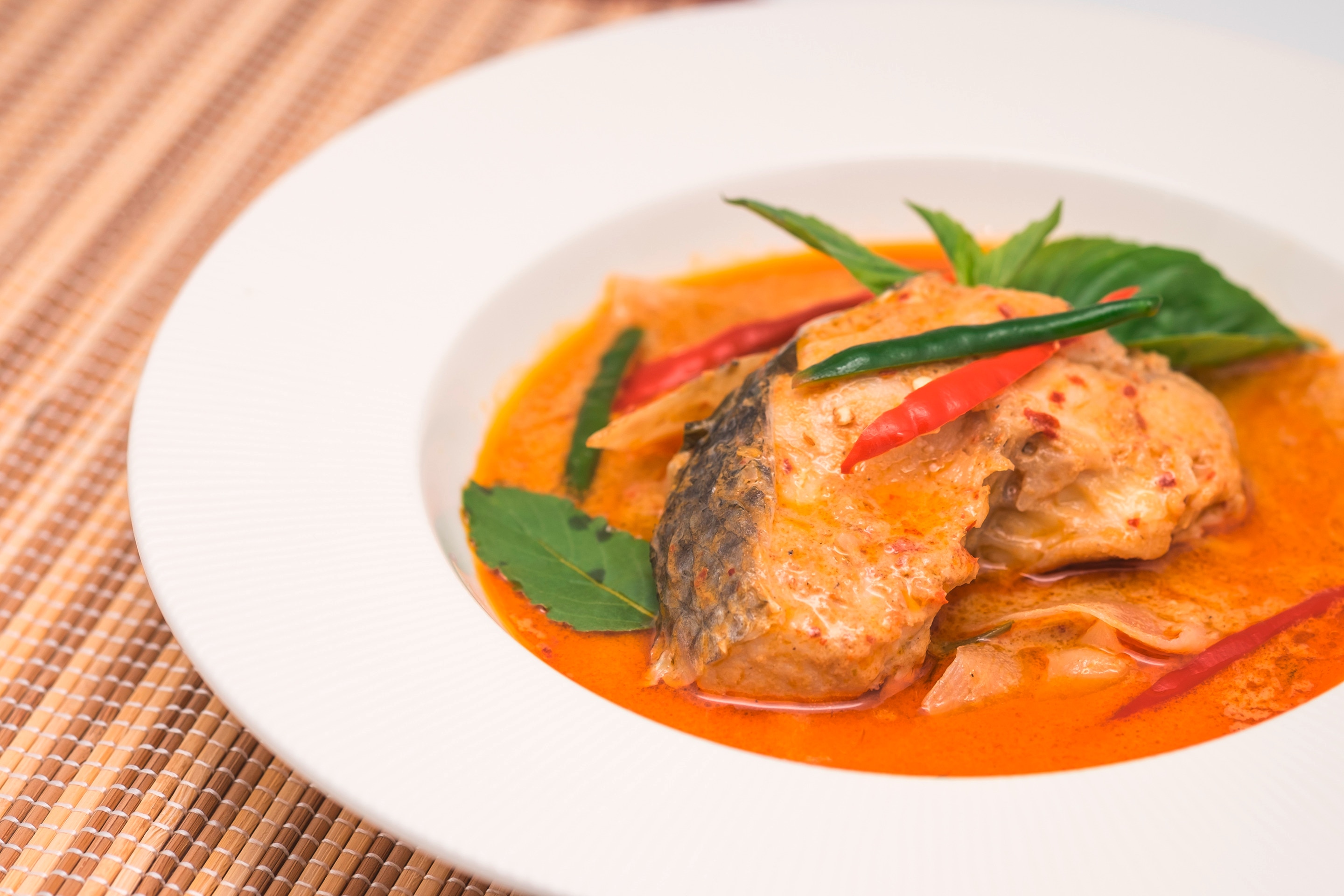 A serving of fish curry garnished with fresh herbs and chilies