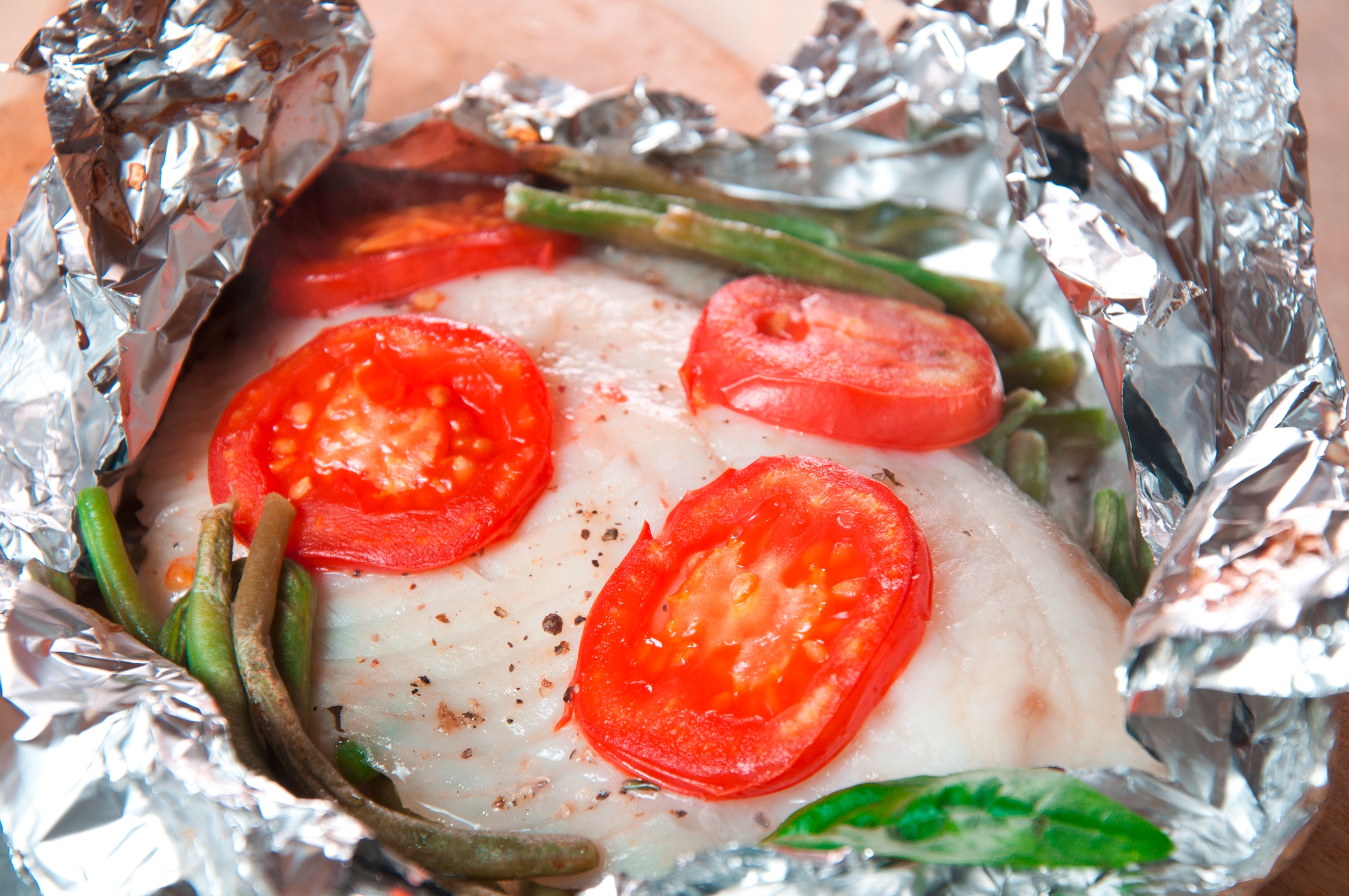 A foil packet of fish fillet topped with vegetables