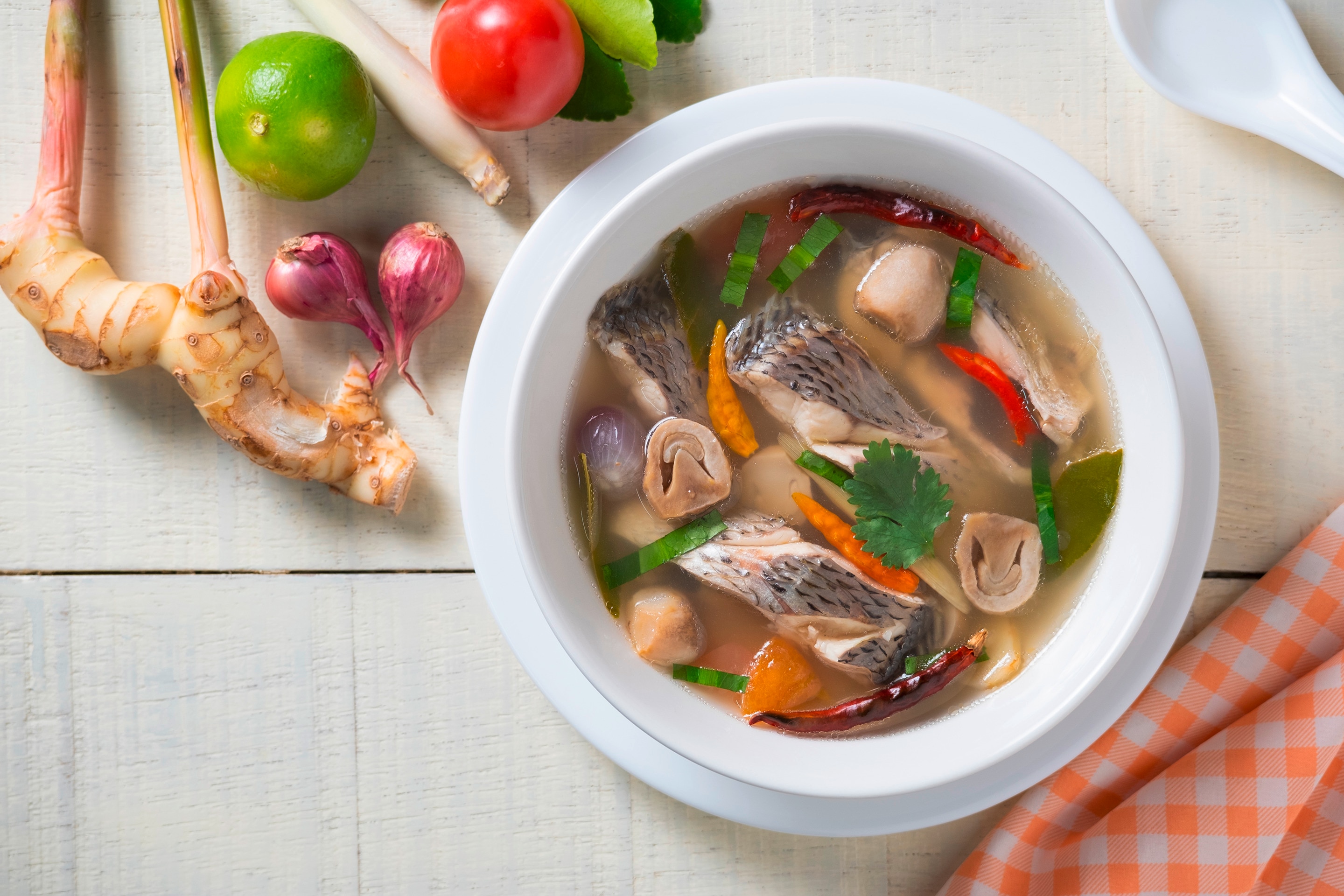 A bowl of tom yum tilapia next to fresh ingredients