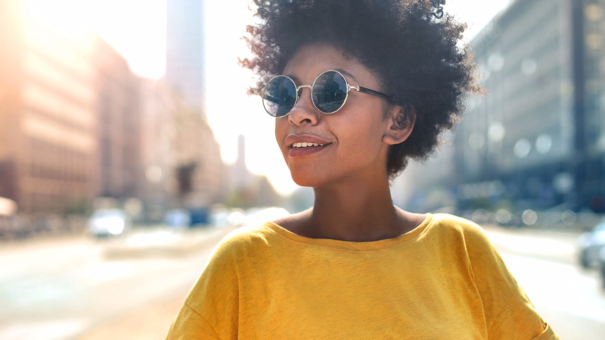 Người phụ nữ đeo kính mắt, mặc áo vàng đang mỉm cười trên phố