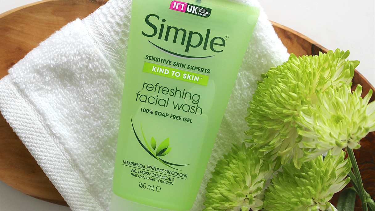 Tube of Simple Refreshing Facial Wash lying on a white face cloth alongside green flowers