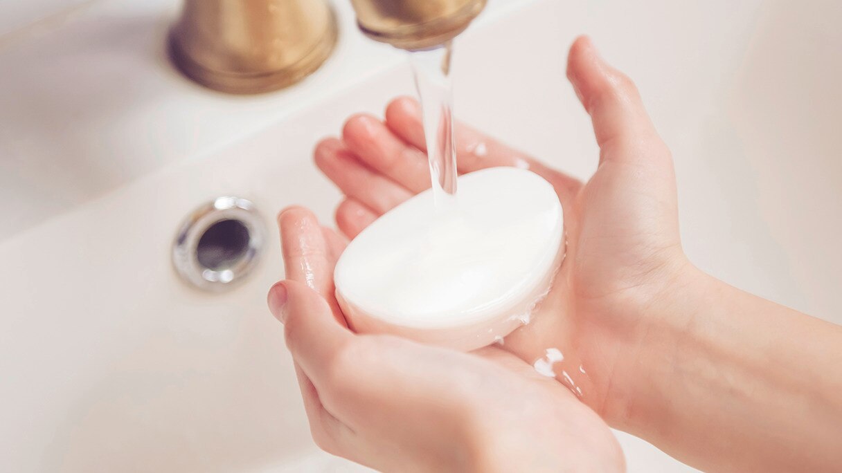Woman holding a bar of soap under running water