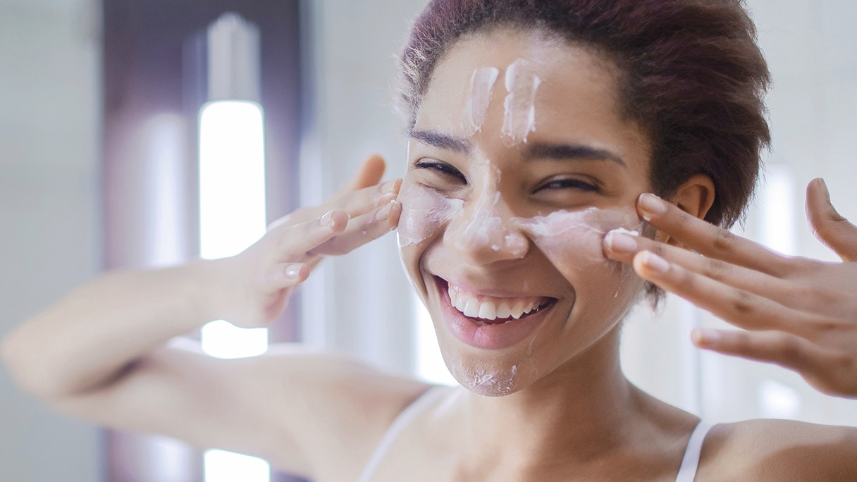 Smiling girl rubbing cream on her cheeks