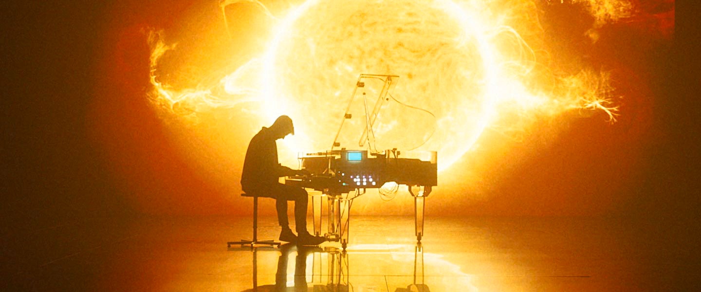 Un uomo che suona il piano davanti ad un video che mostra l'esplosione del sole 