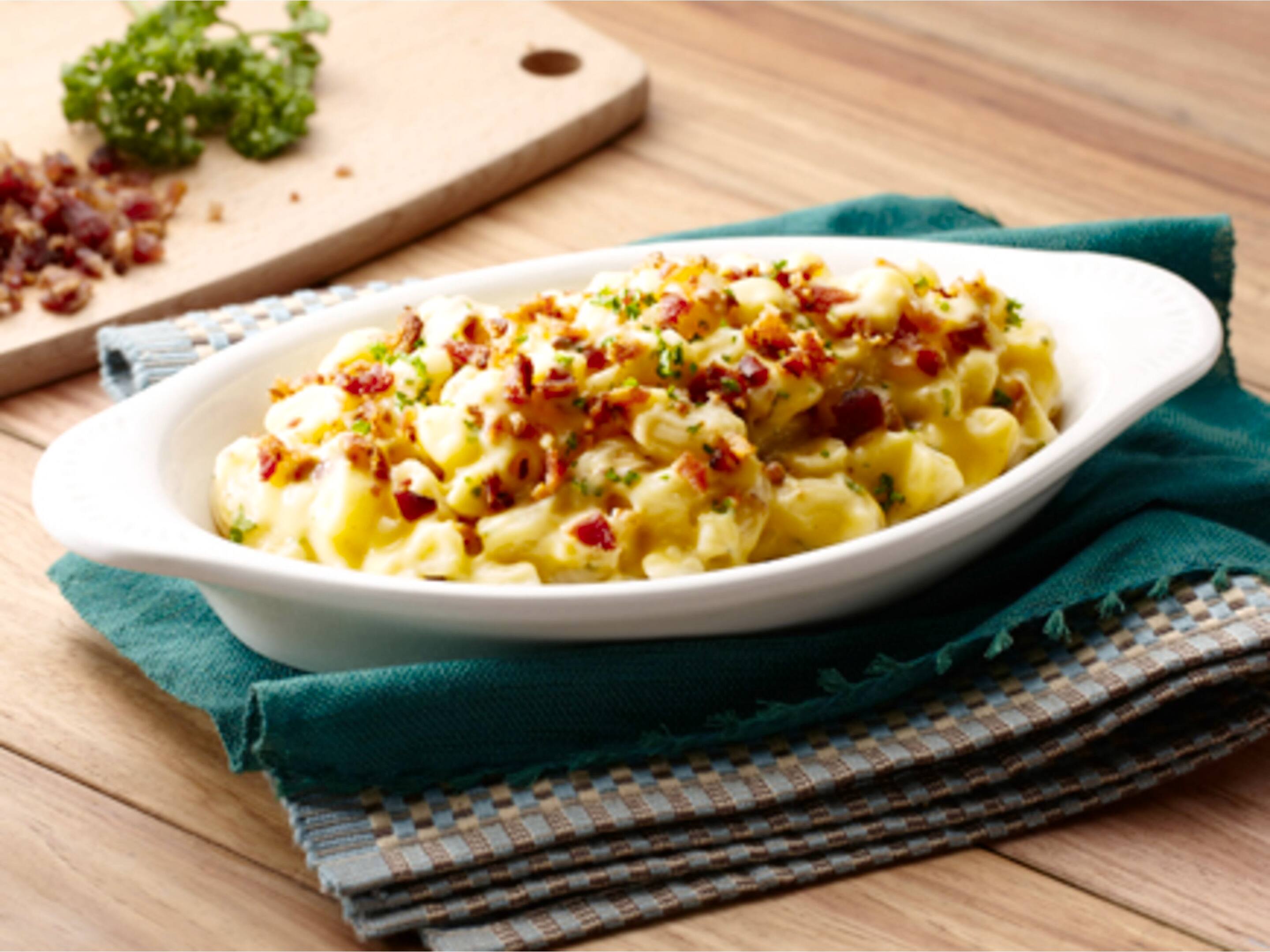 Mac and Cheese with bacon bits and parsley for garnish on a wooden table