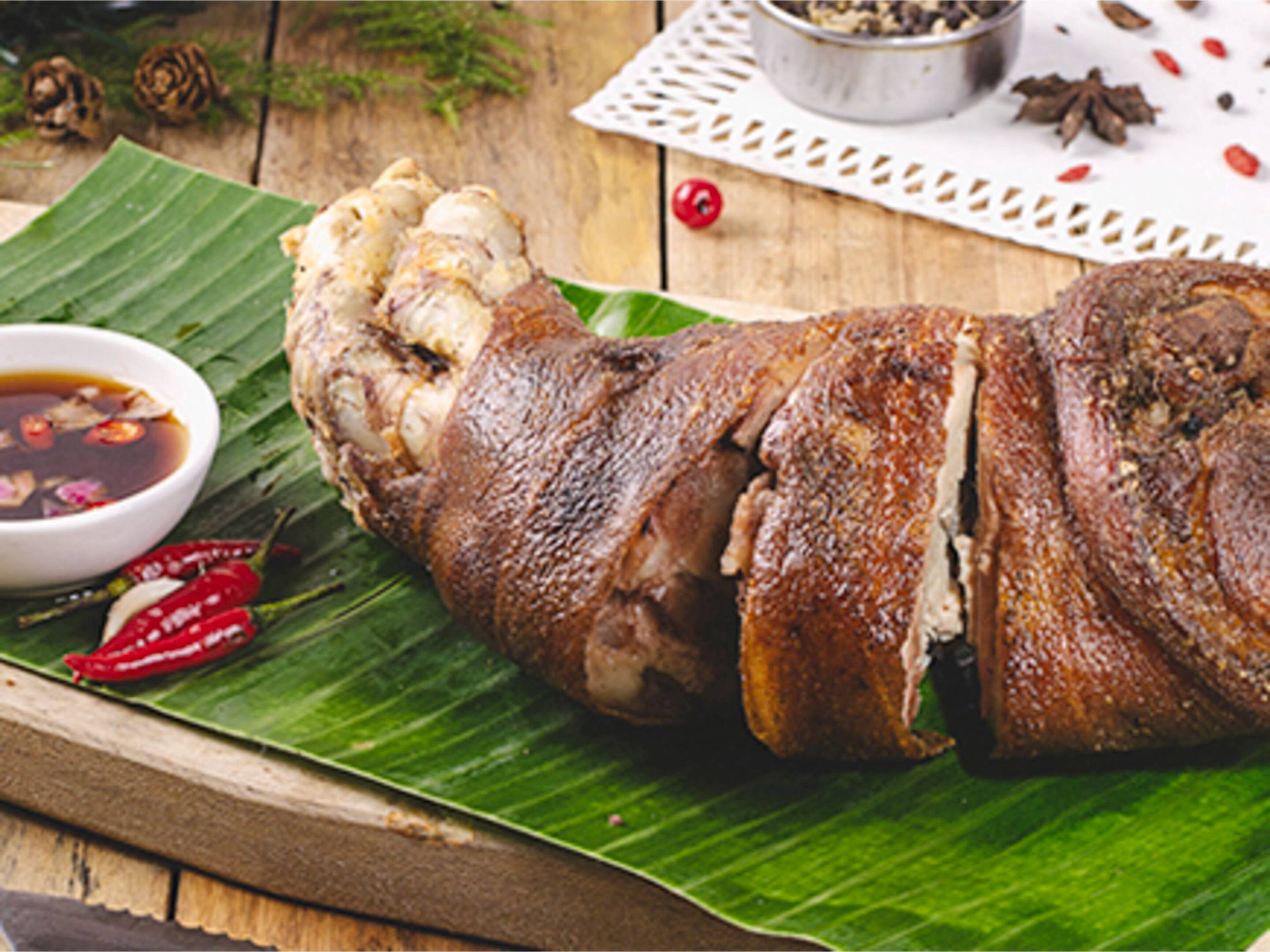 Whole crispy pata leg on a banana leaf served with soy sauce dipping sauce