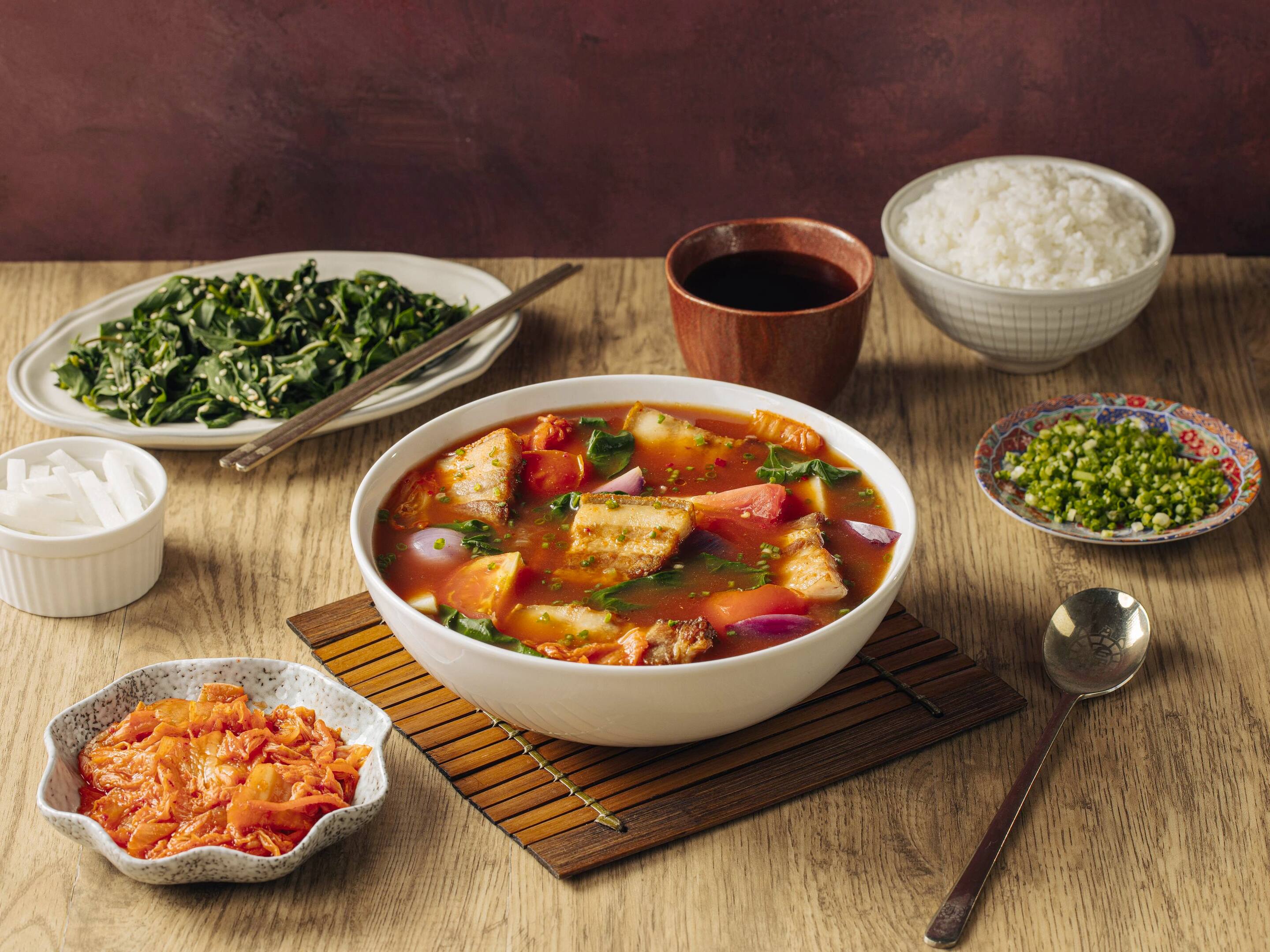 A bowl of kimchi sinigang served with Korean side dishes, including rice