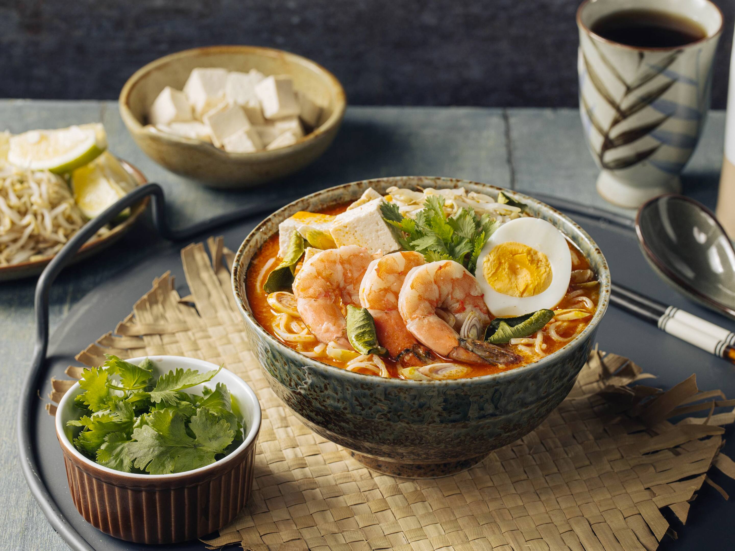A bowl of laksa topped with shrimps, tofu, hard-boiled eggs, and fresh cilantro