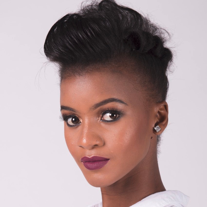 Model with purple lipstick, dark skin tone and short dark brown hair in a high upstyle