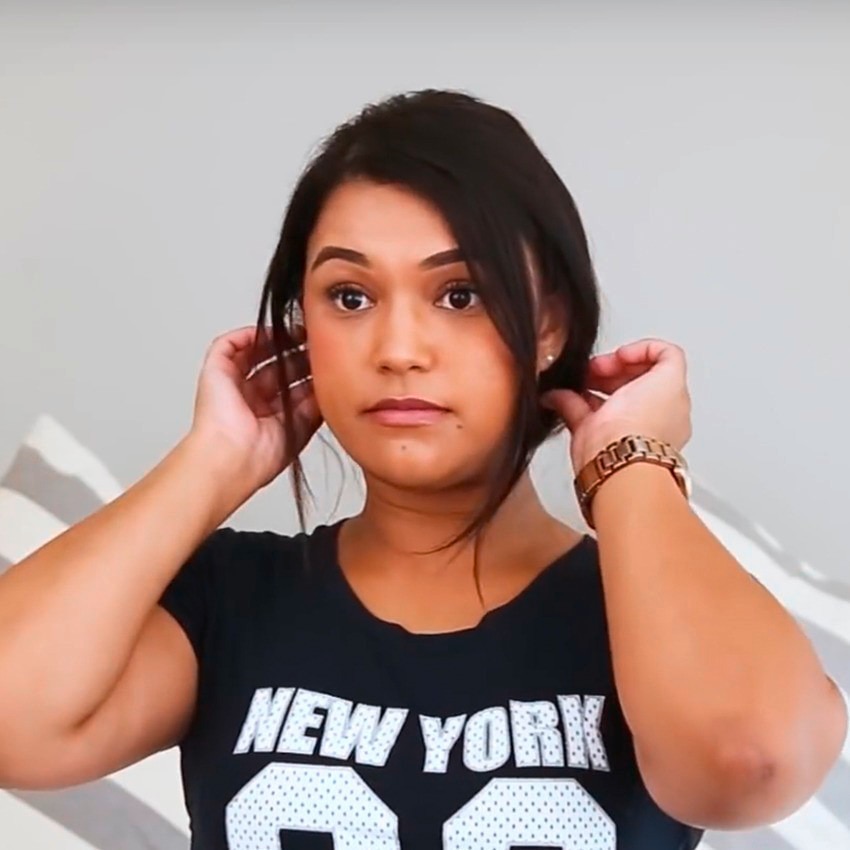 Blogger wearing a black and white "New York" T-shirt and a gold watch, holding the back pieces of her hair on either side of her head with either hand