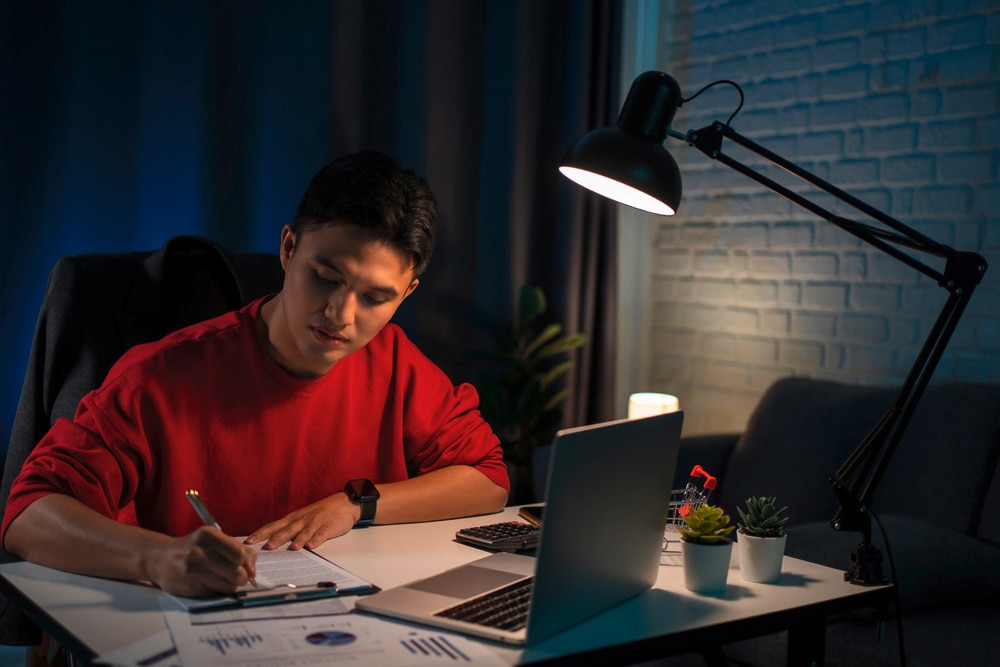 Man in red sweater working on his desk at night.