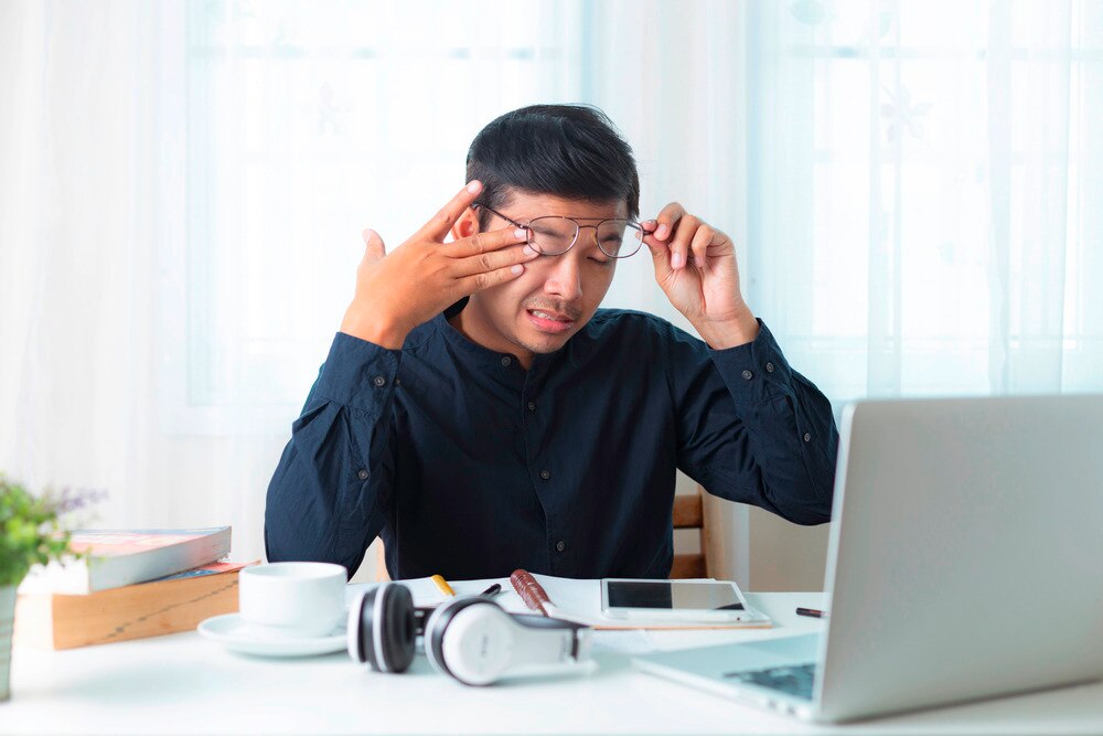 Overwhelmed Asian man rubbing his eyes under his glasses.