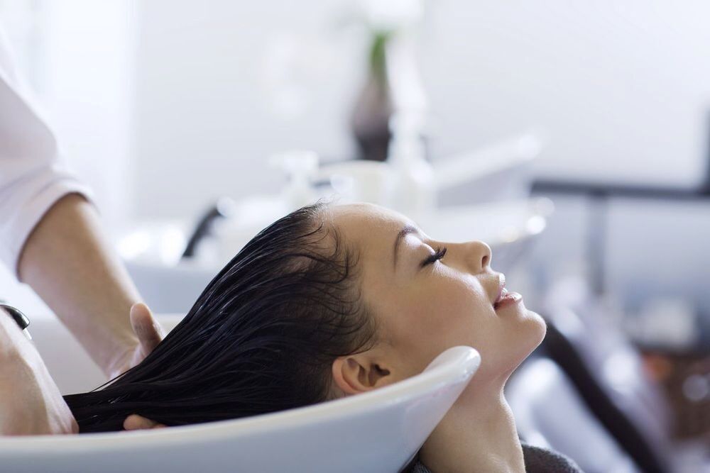 Asian woman happily getting her hair washed by a hairstylist.