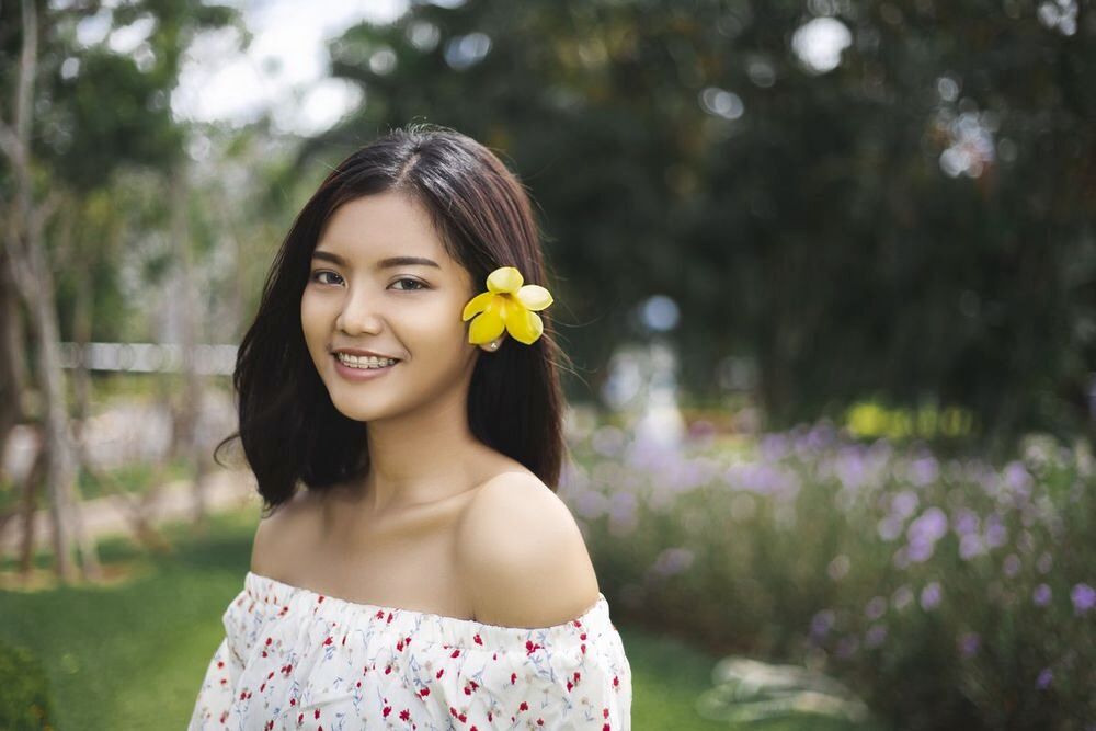 Asian woman with a flower pinned to her shoulder length hair.