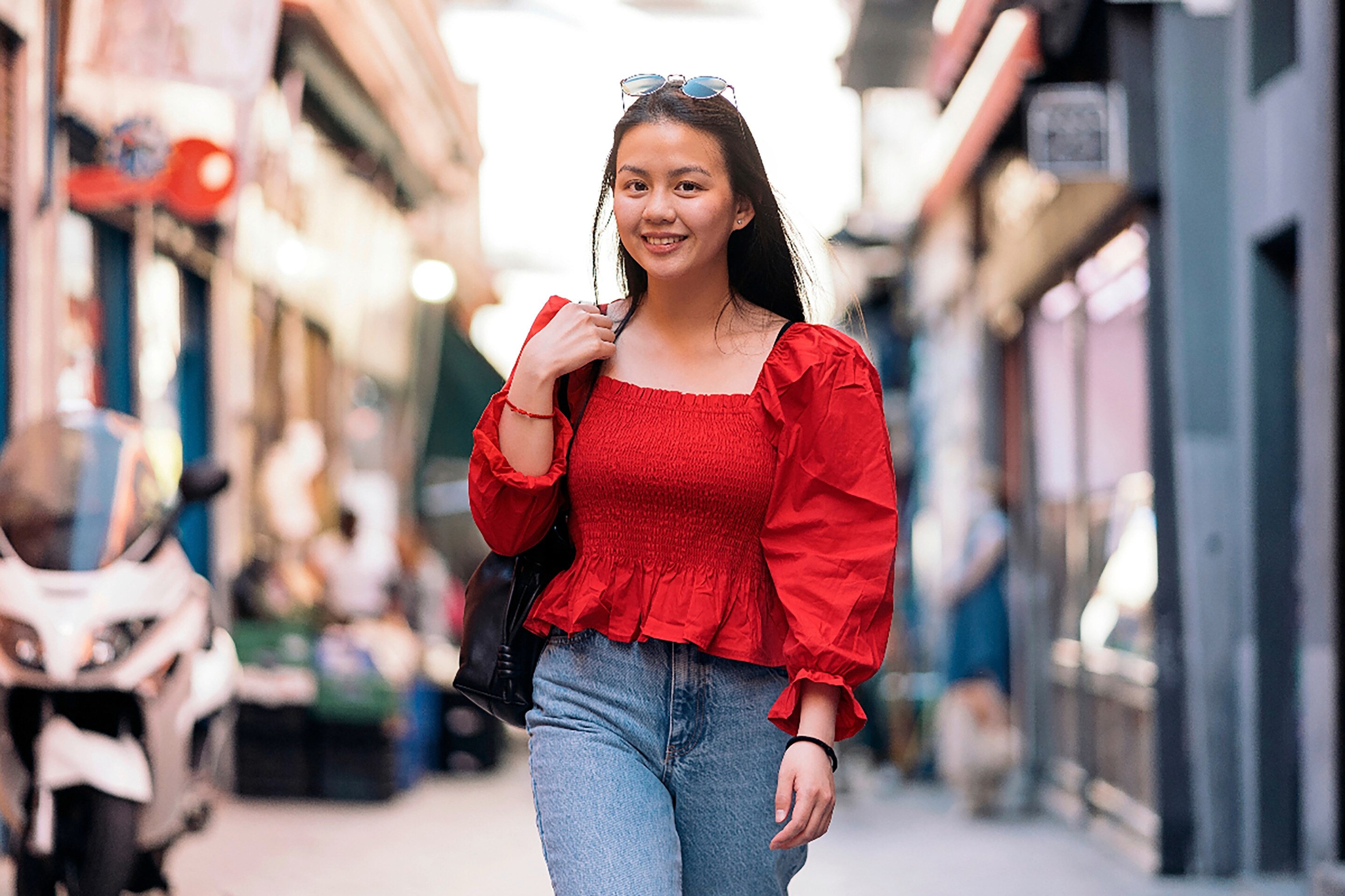 Woman in red top and denim pants confidently walking toward the camera.