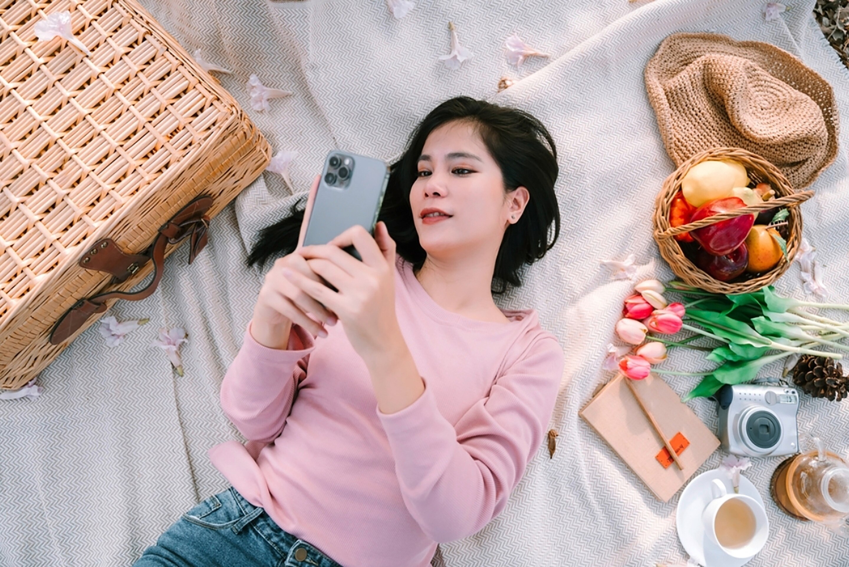 Woman wearing pink sweater lying on a white sheet while picnicking.