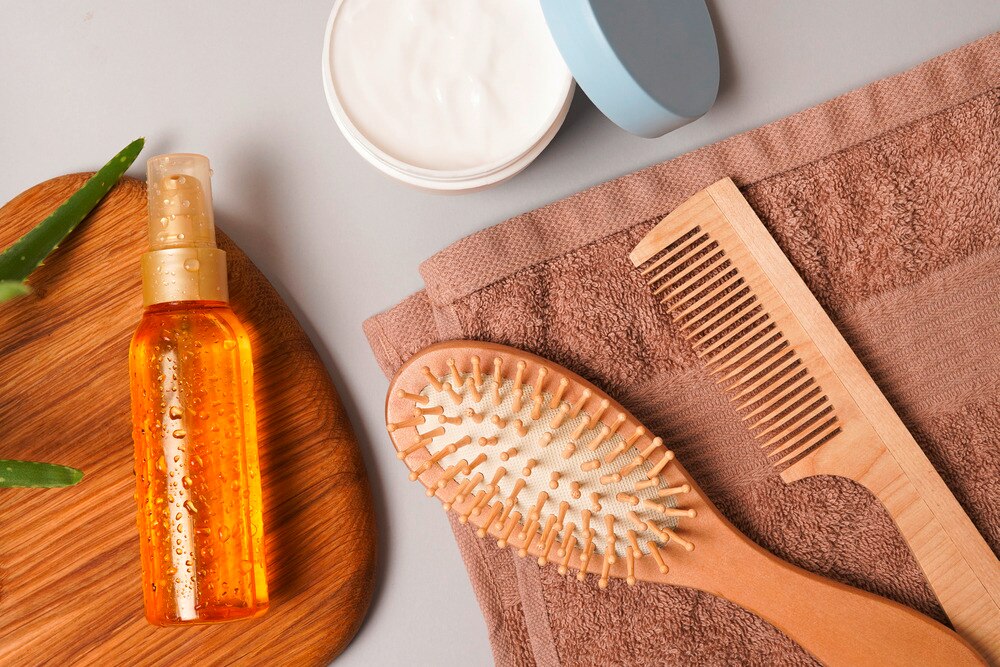 Photo of haircare tools including a brush, comb, hair oil, hair mask, and a towel.