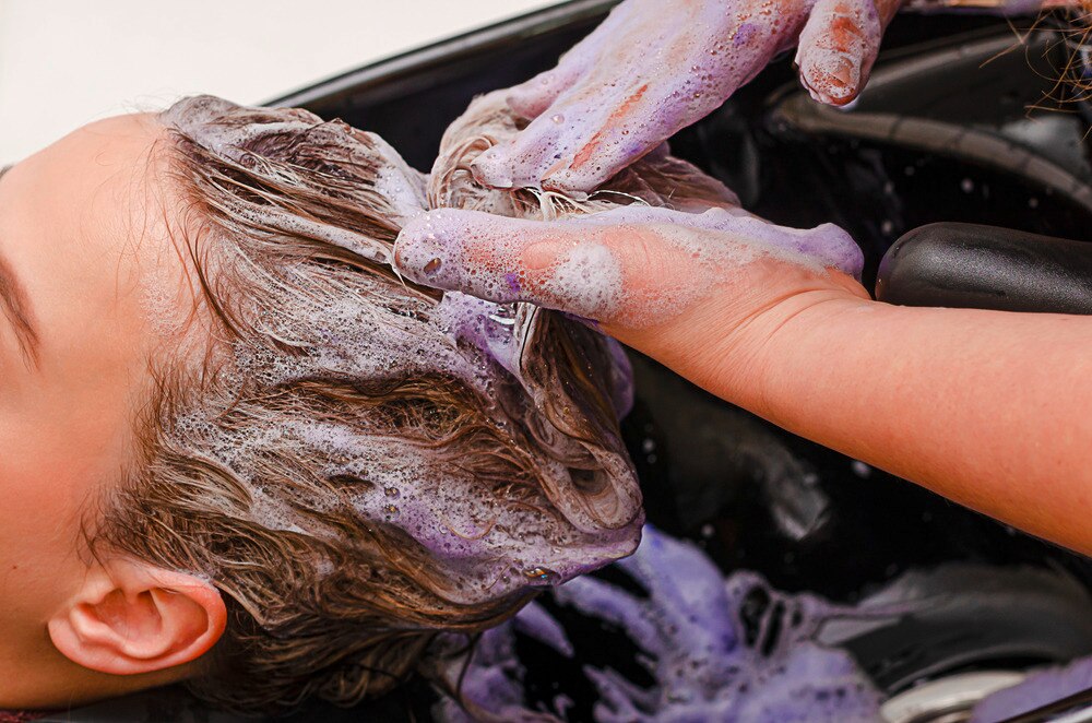 Closeup of a hands using purple shampoo on bleached hair.
