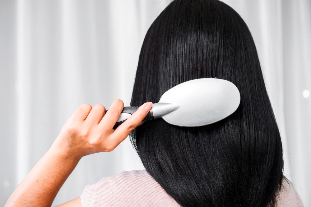 Woman brushing her long black hair with silver padded brush.