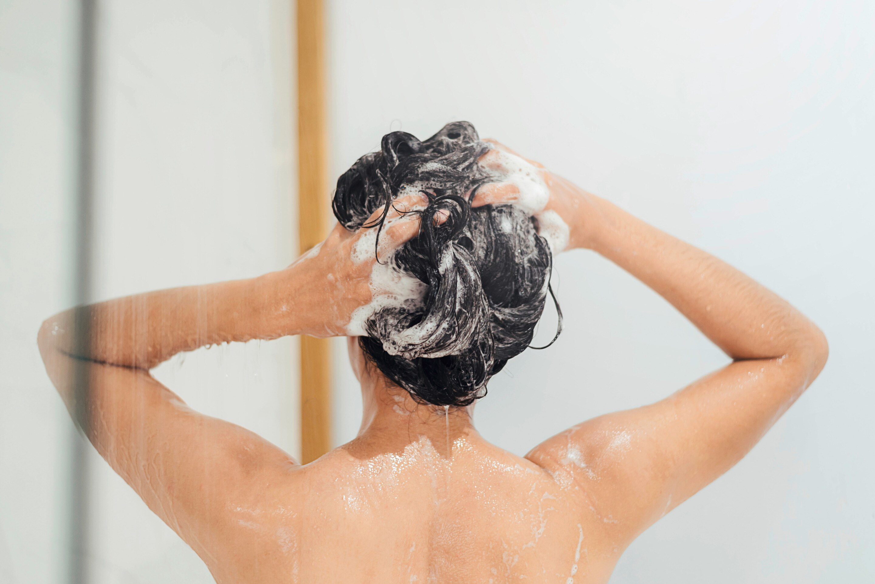 Woman with her back turned, shampooing her hair. 