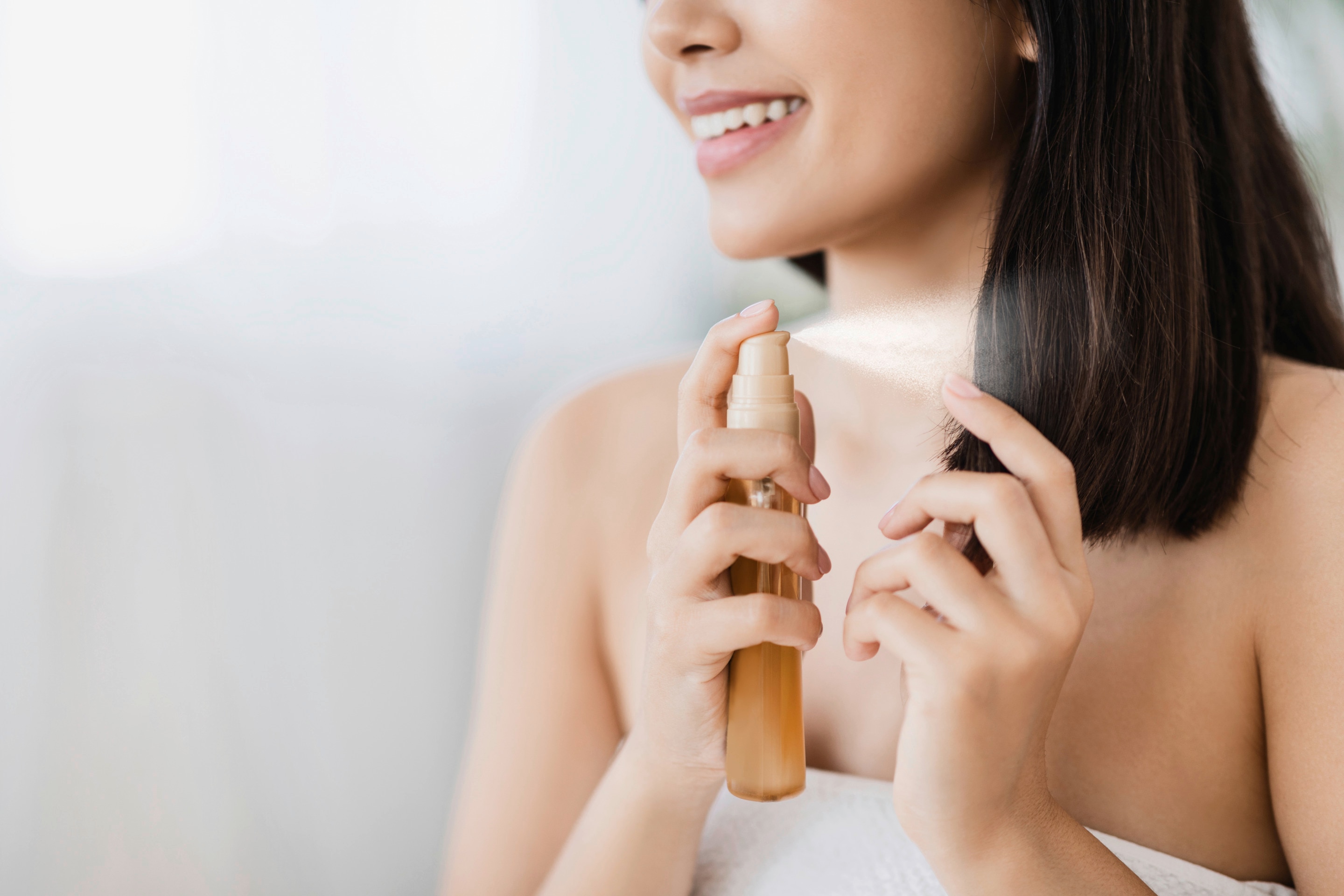 Closeup of Asian woman spraying treatment on her hair against a white background. 