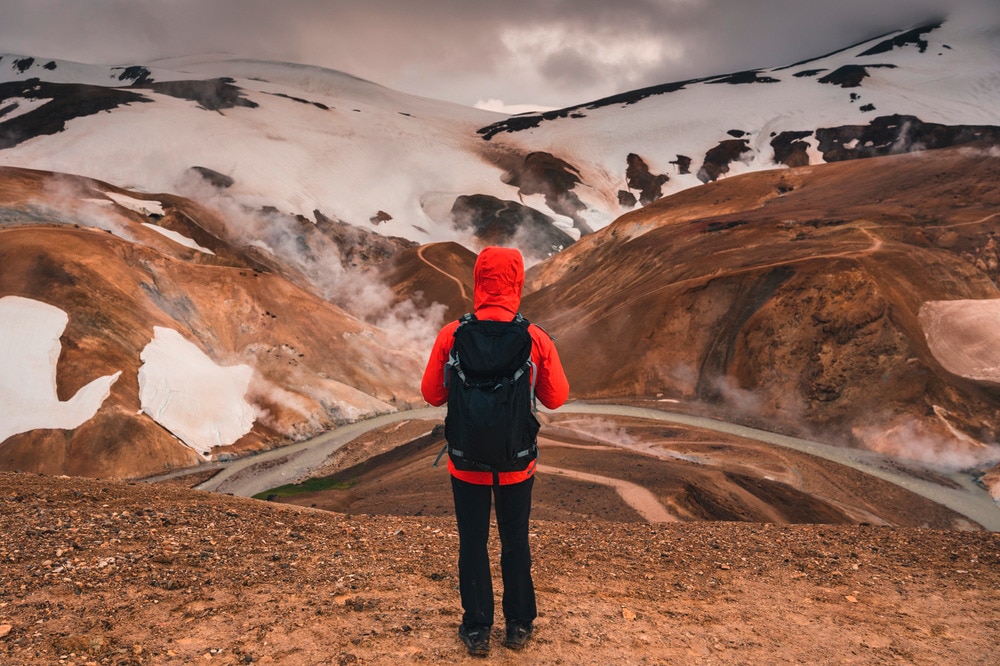 Back of an Asian man in a red jacket and black backpack hiking.