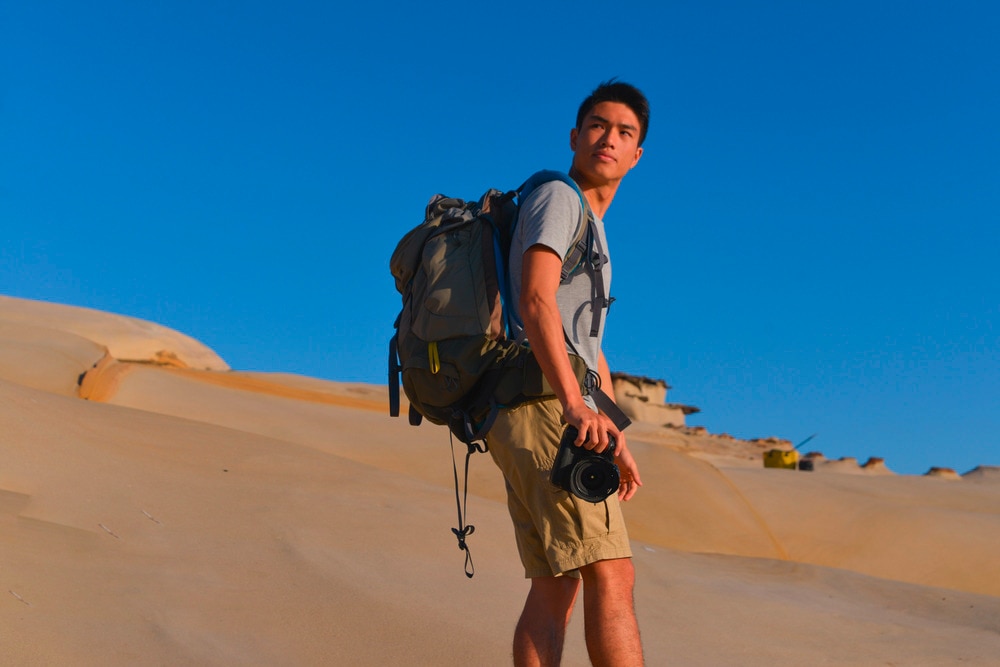 Asian man with a backpack and a camera in the desert