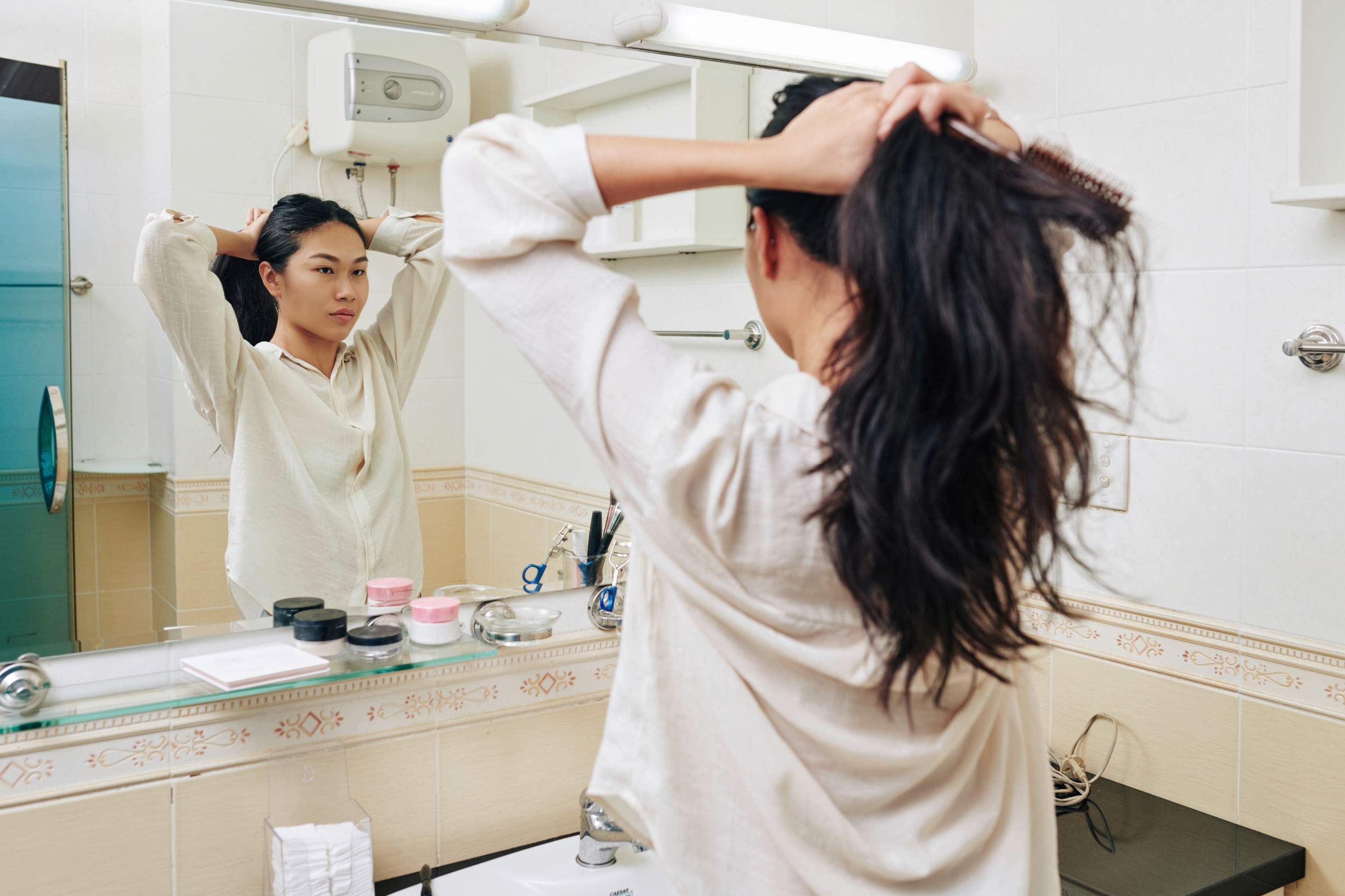 Asian woman tying her hair in front of a mirror.
