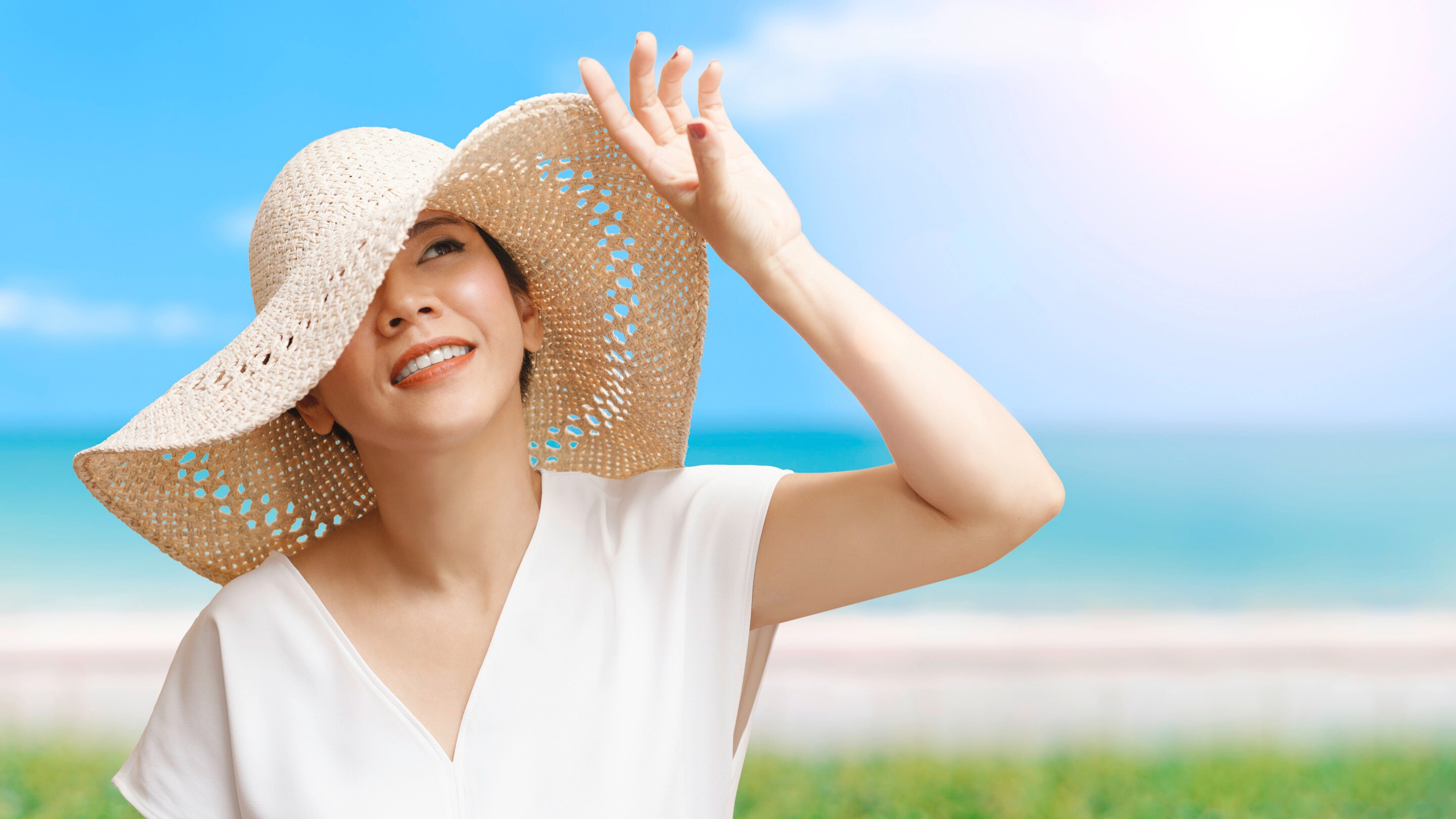 Asian woman at the beach wearing a wide brimmed hat blocking her face from the sun.