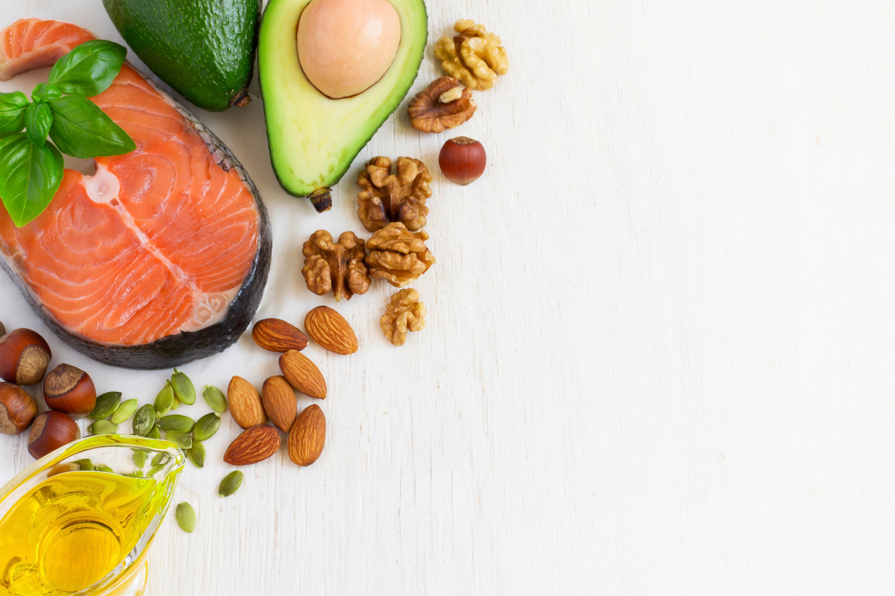 Flat lay of salmon, nuts, avocado, and oil against a white background. 