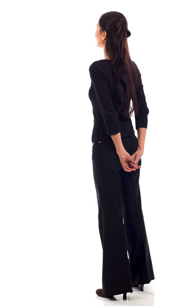 Asian woman in black suit with hands behind back.