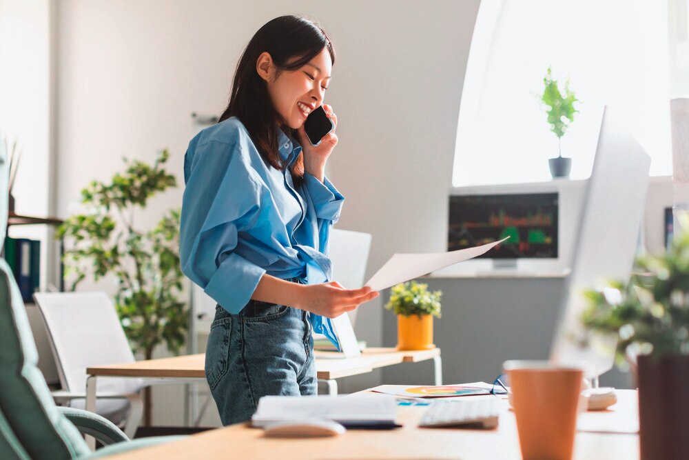 Smiling woman talking on the phone while holding a piece of paper.