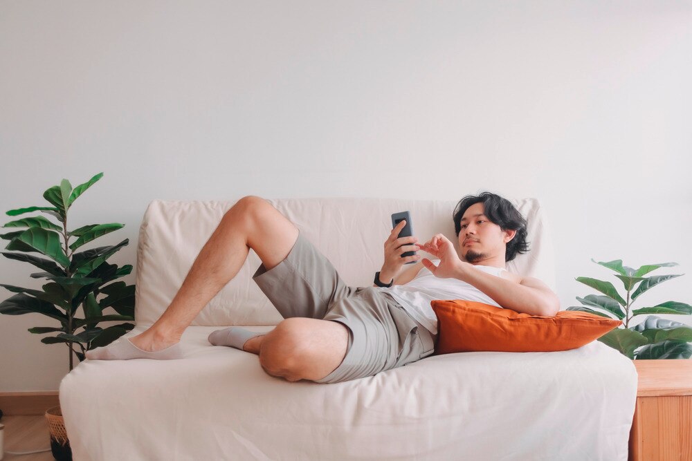 Man lounging on the sofa while playing on his phone.