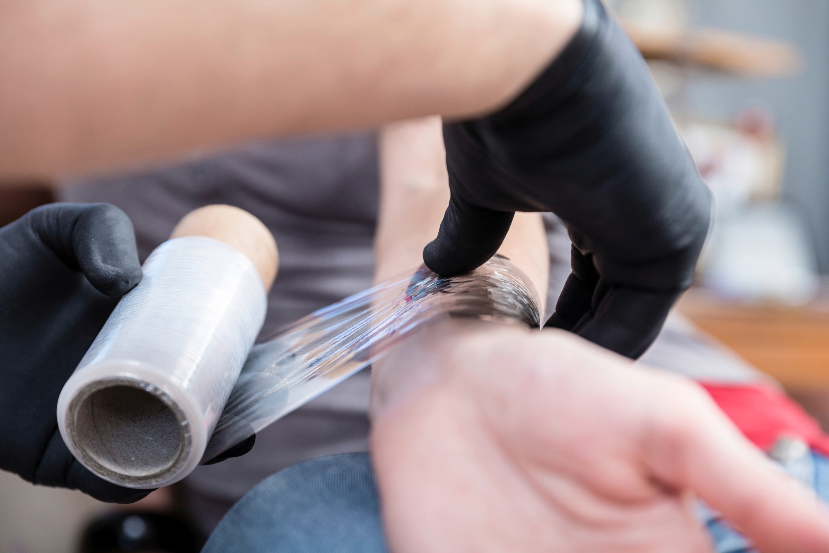 Closeup of tattoo artist’s hands applying film over a new tattoo