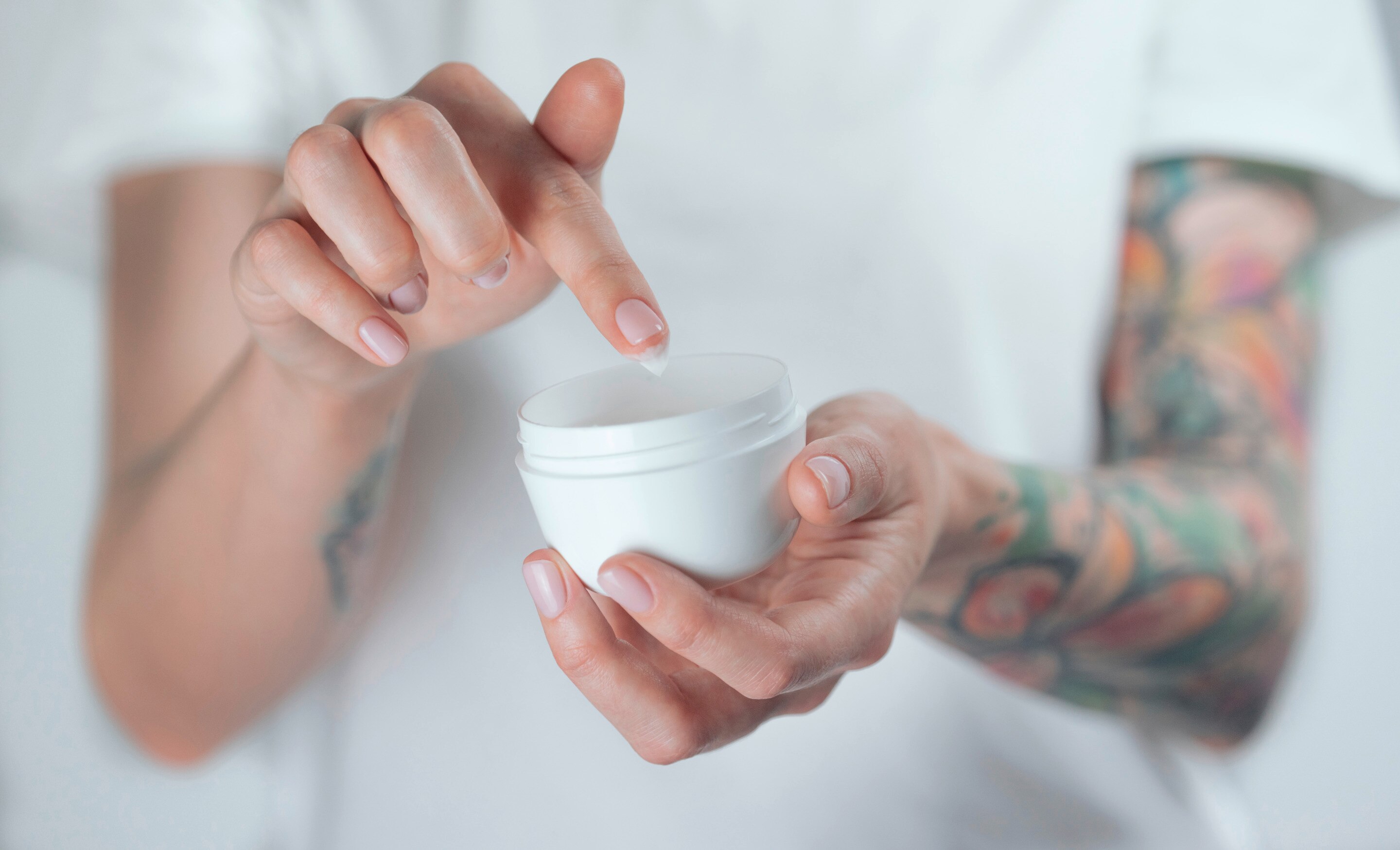 Woman with tattoos holding a jar of moisturizer