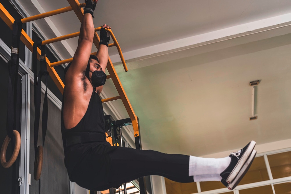 Man with black medical mask doing hanging leg raises.